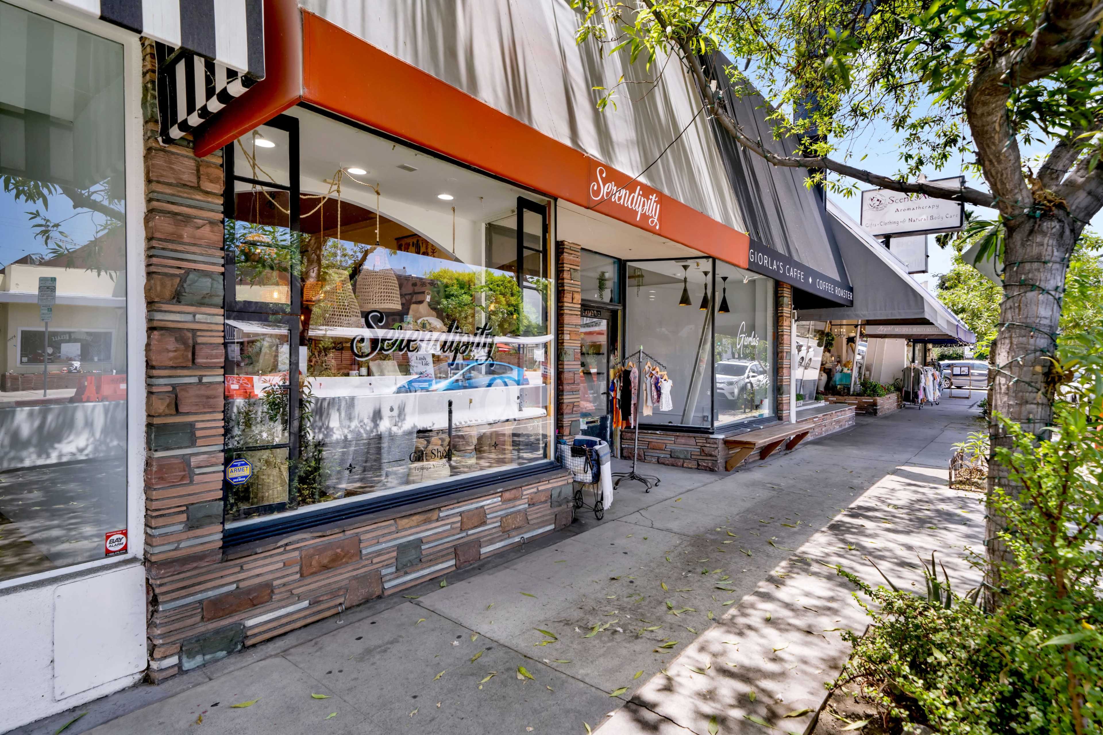 A storefront named "Sew Stylish" is visible, featuring large windows and a canopy, alongside a tree-lined sidewalk with other shops in the background.