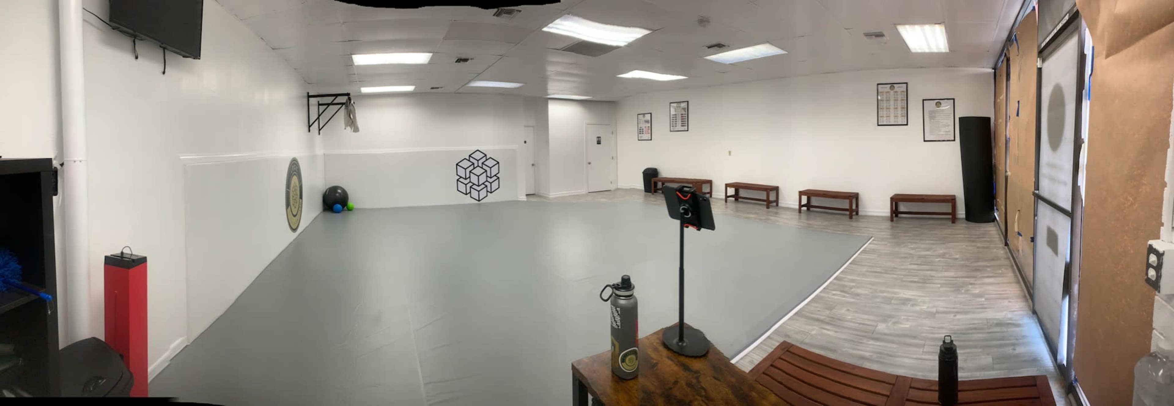 A spacious, empty gym or workout studio with gray flooring, benches along the walls, and exercise equipment in one corner.