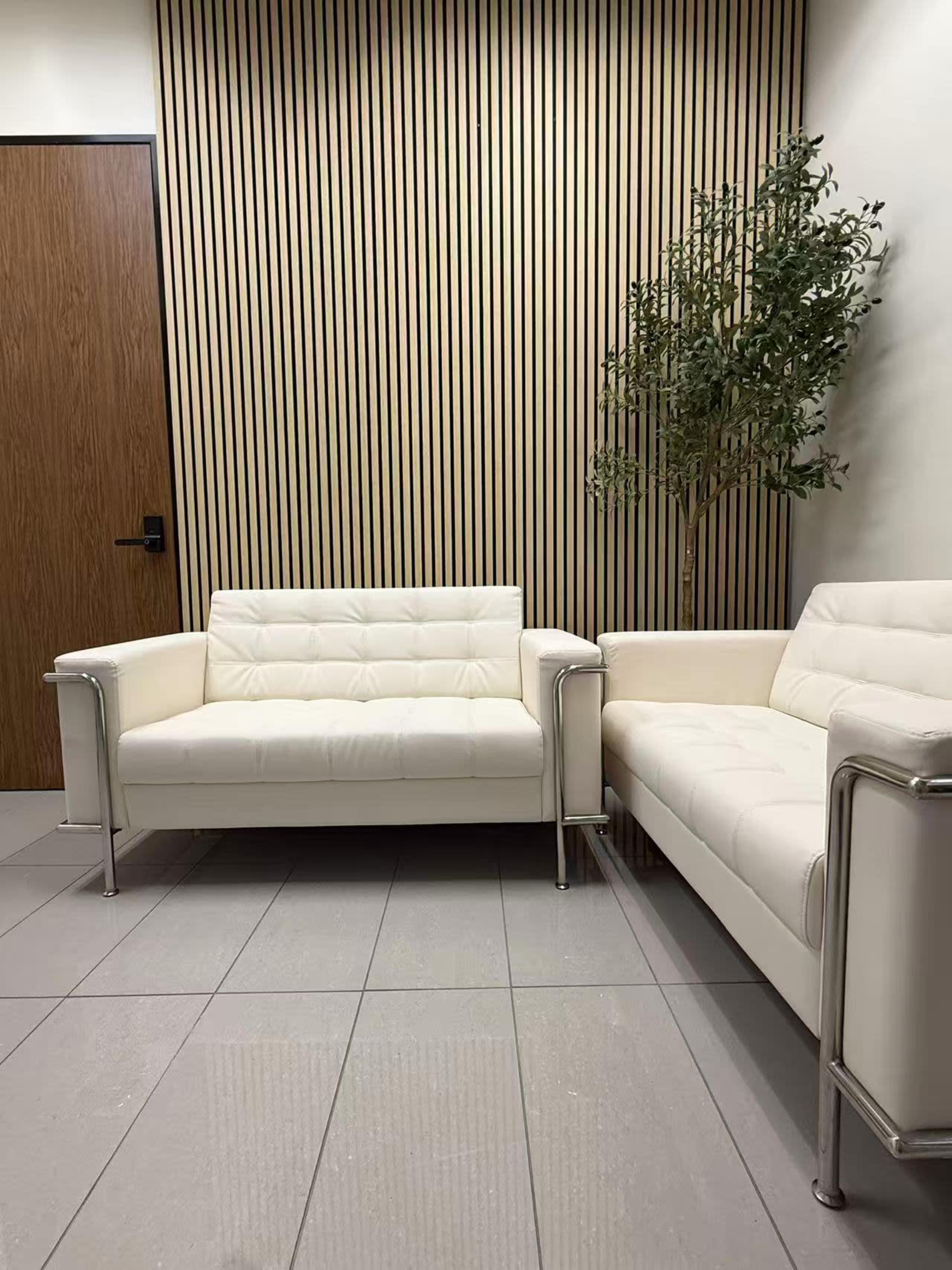 The image shows a seating area with two white sofas positioned against a wall featuring vertical wooden panels, alongside a small potted plant.