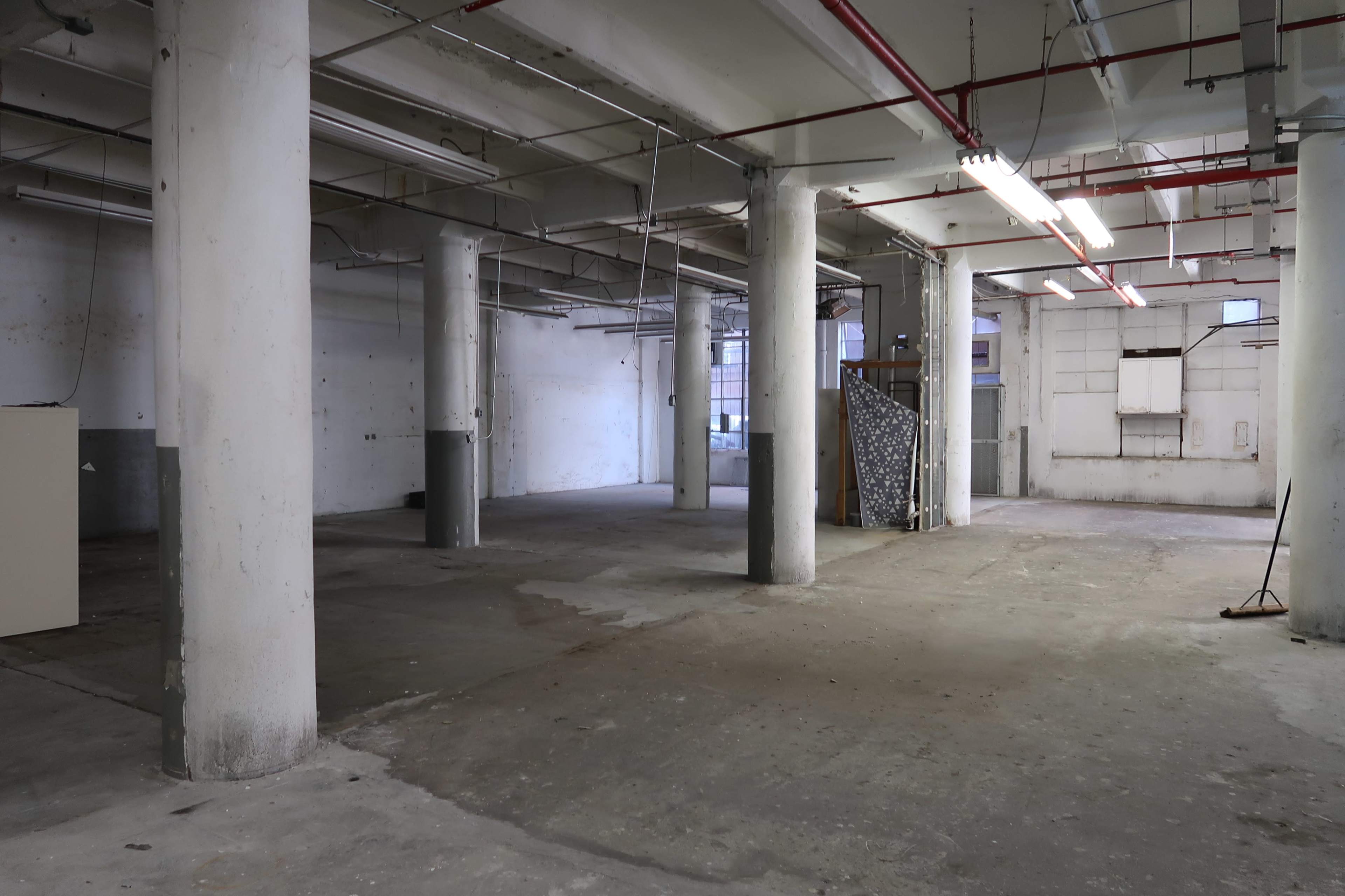 An empty industrial space with concrete flooring, exposed pillars, and bare walls.