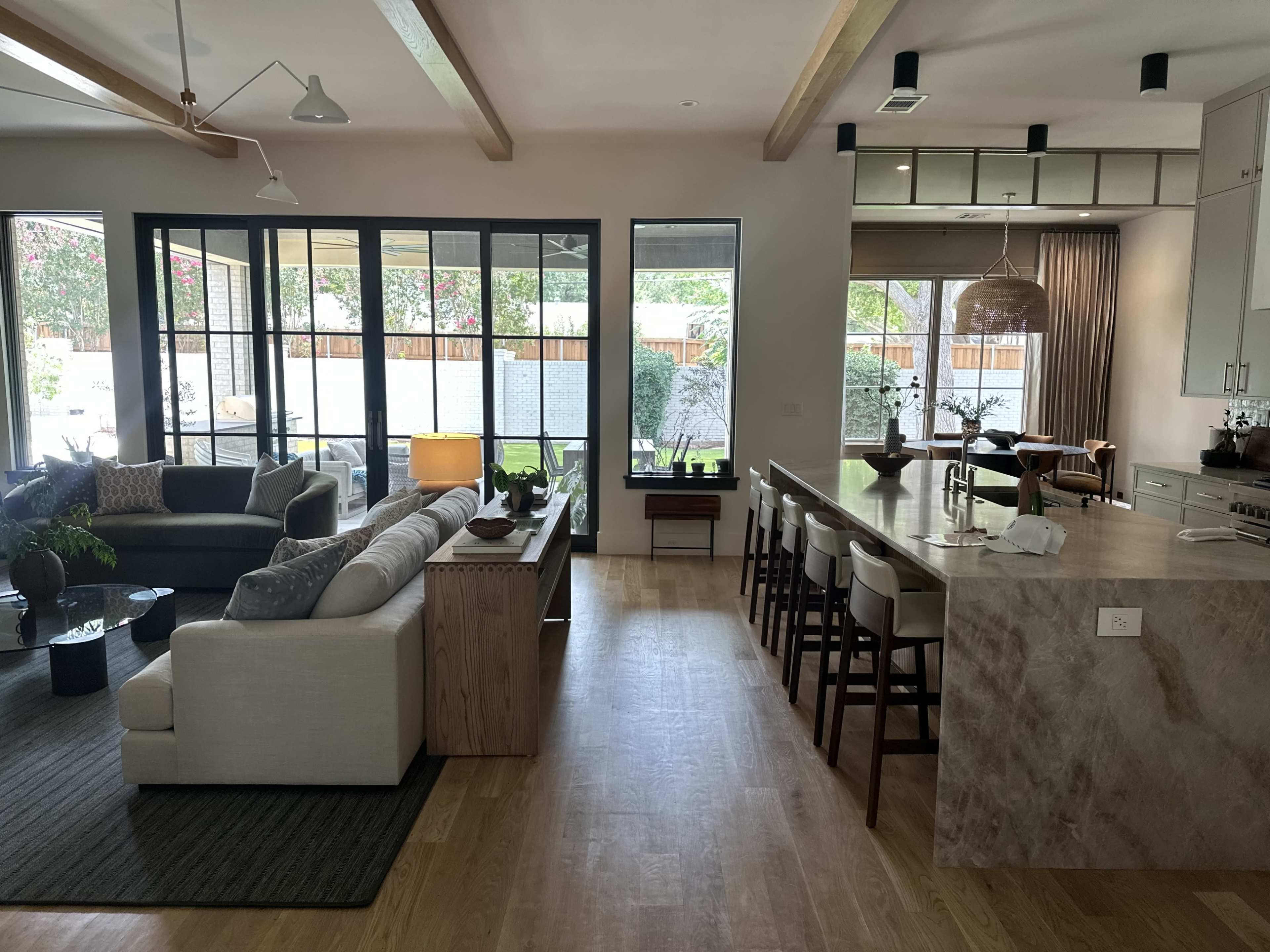 The image shows a modern open-concept living space with a living area, kitchen island, and large windows allowing natural light.