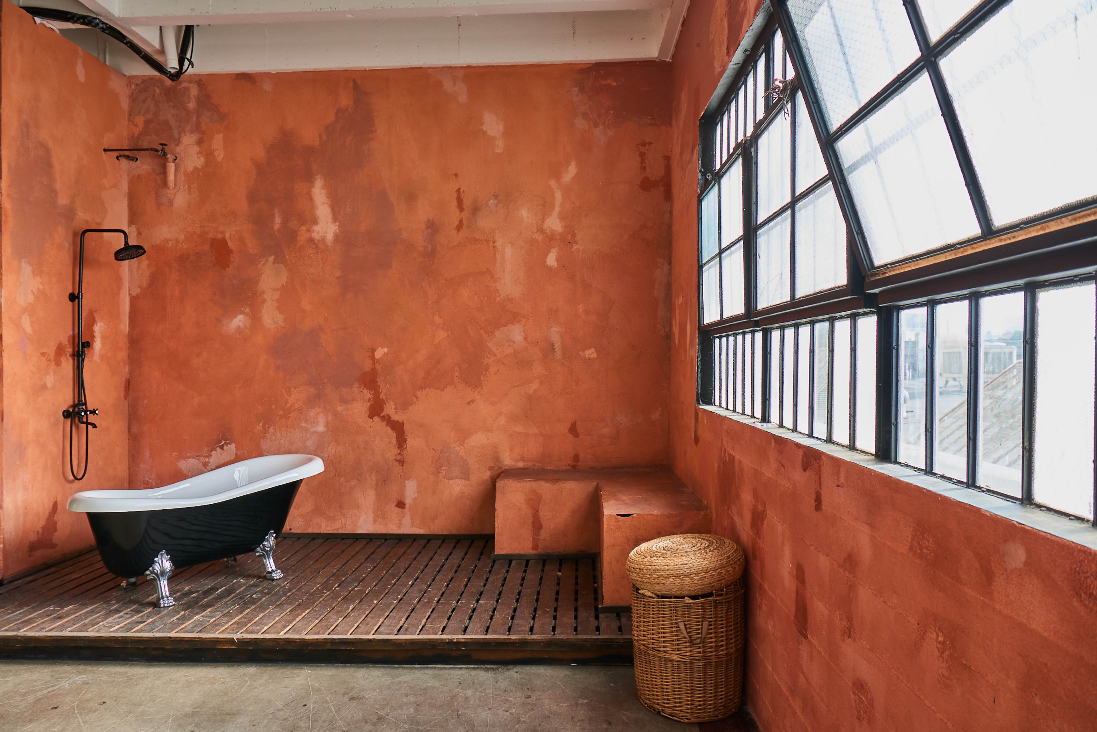 A bathroom with an orange wall, a black freestanding bathtub, a shower fixture, and a woven basket near the window.