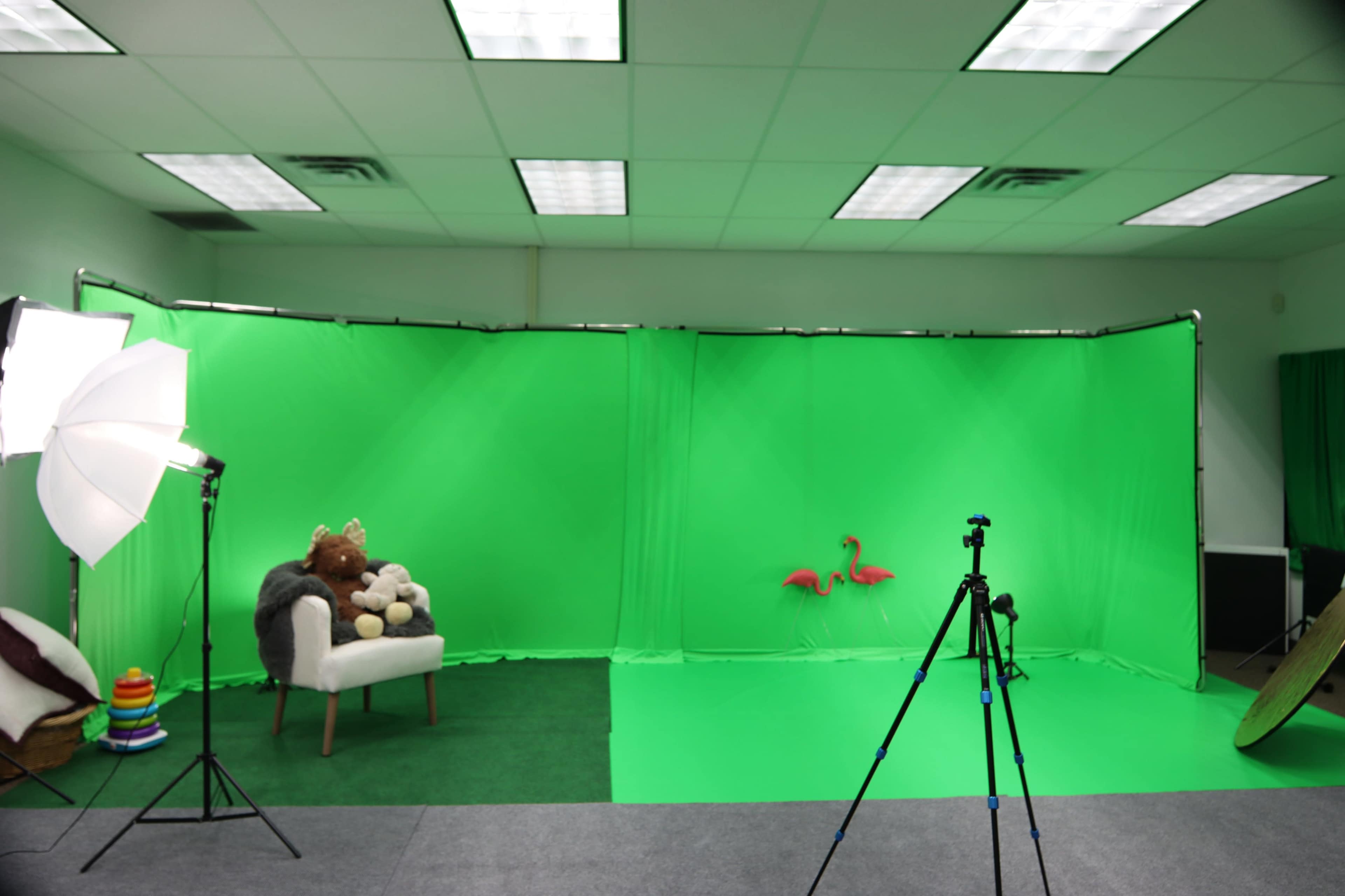 A studio setup features a green screen backdrop with a chair, plush toys, and equipment for photography or video production.