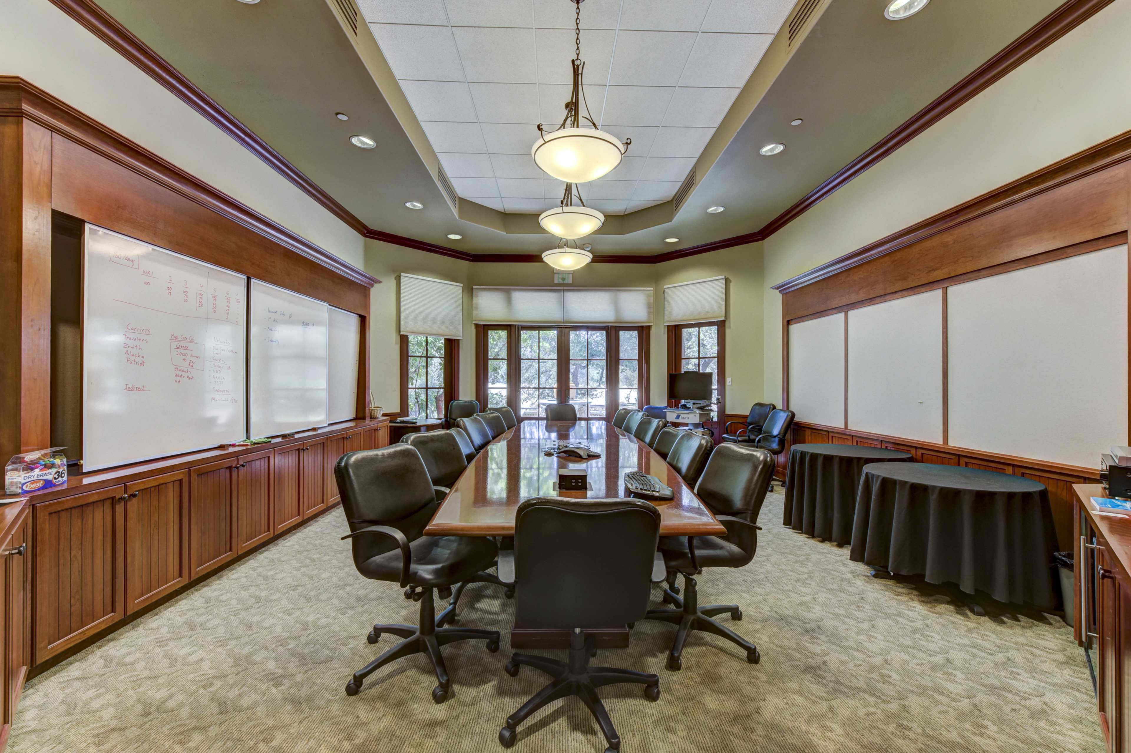 A well-furnished conference room with a large wooden table surrounded by black office chairs and whiteboards on the walls.