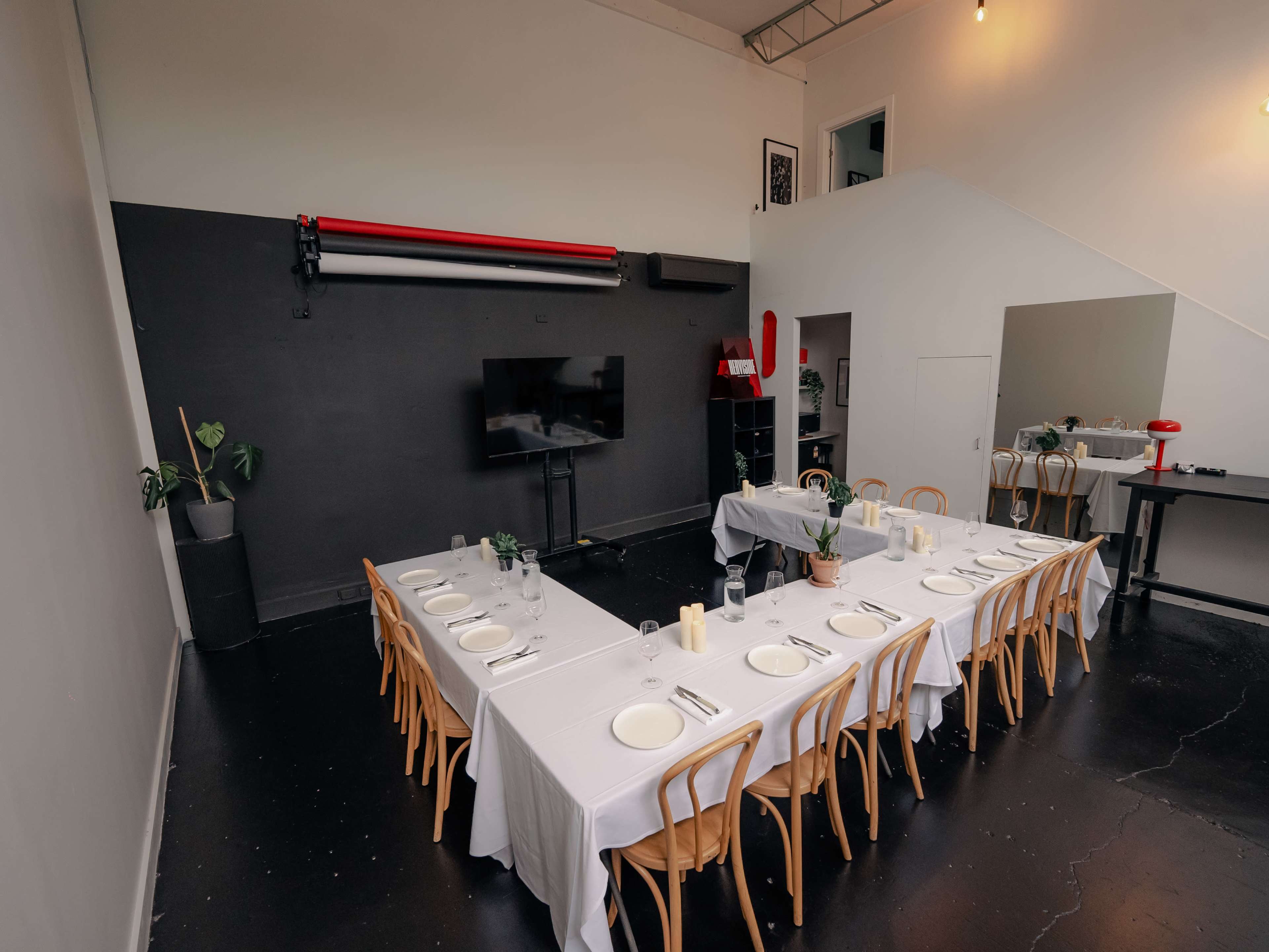 A long table set for a meal with white tablecloths and chairs in a modern, minimally decorated indoor space.