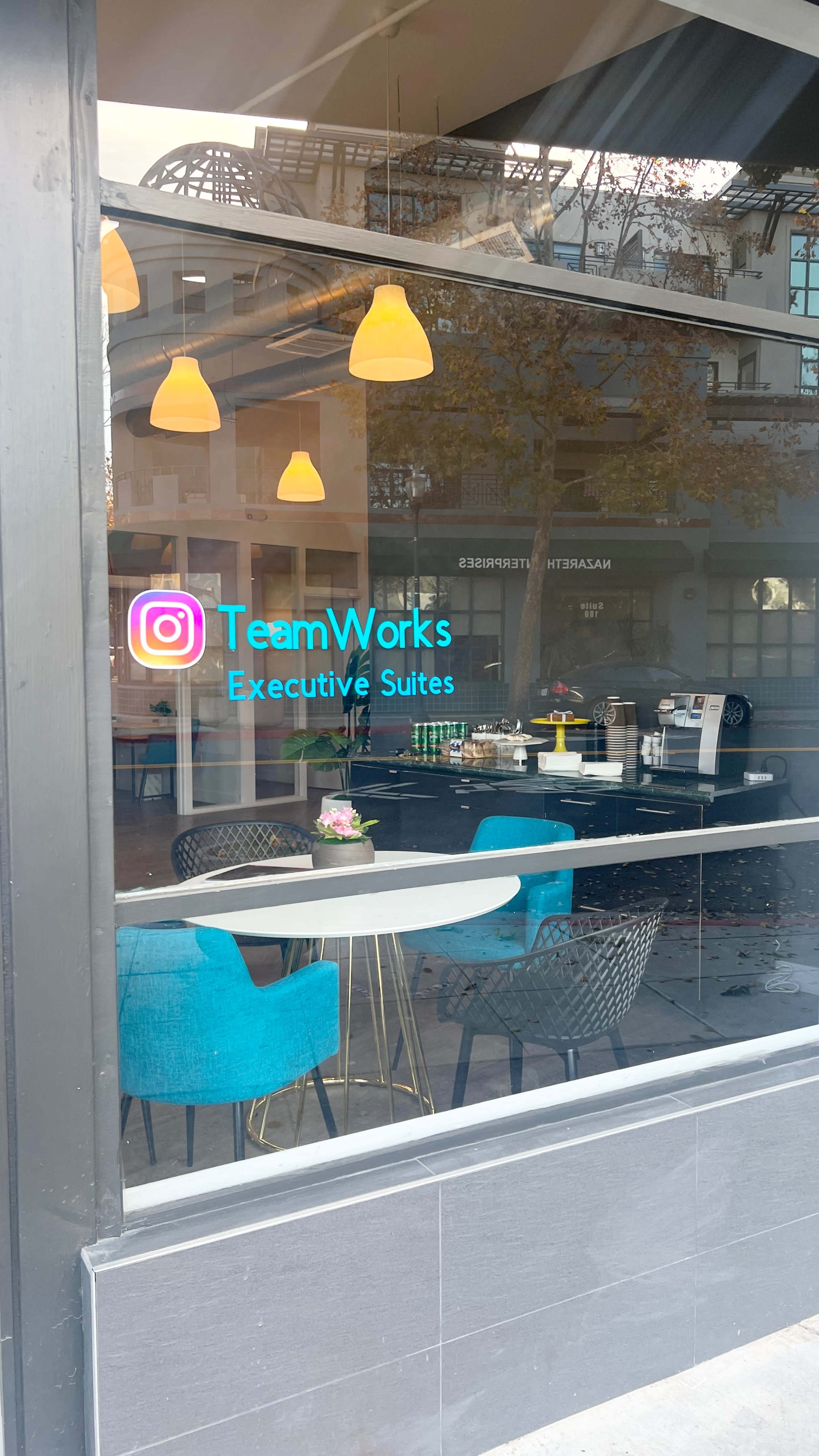 A modern office space with brightly colored chairs and a display for "TeamWorks Executive Suites" visible through a large window.