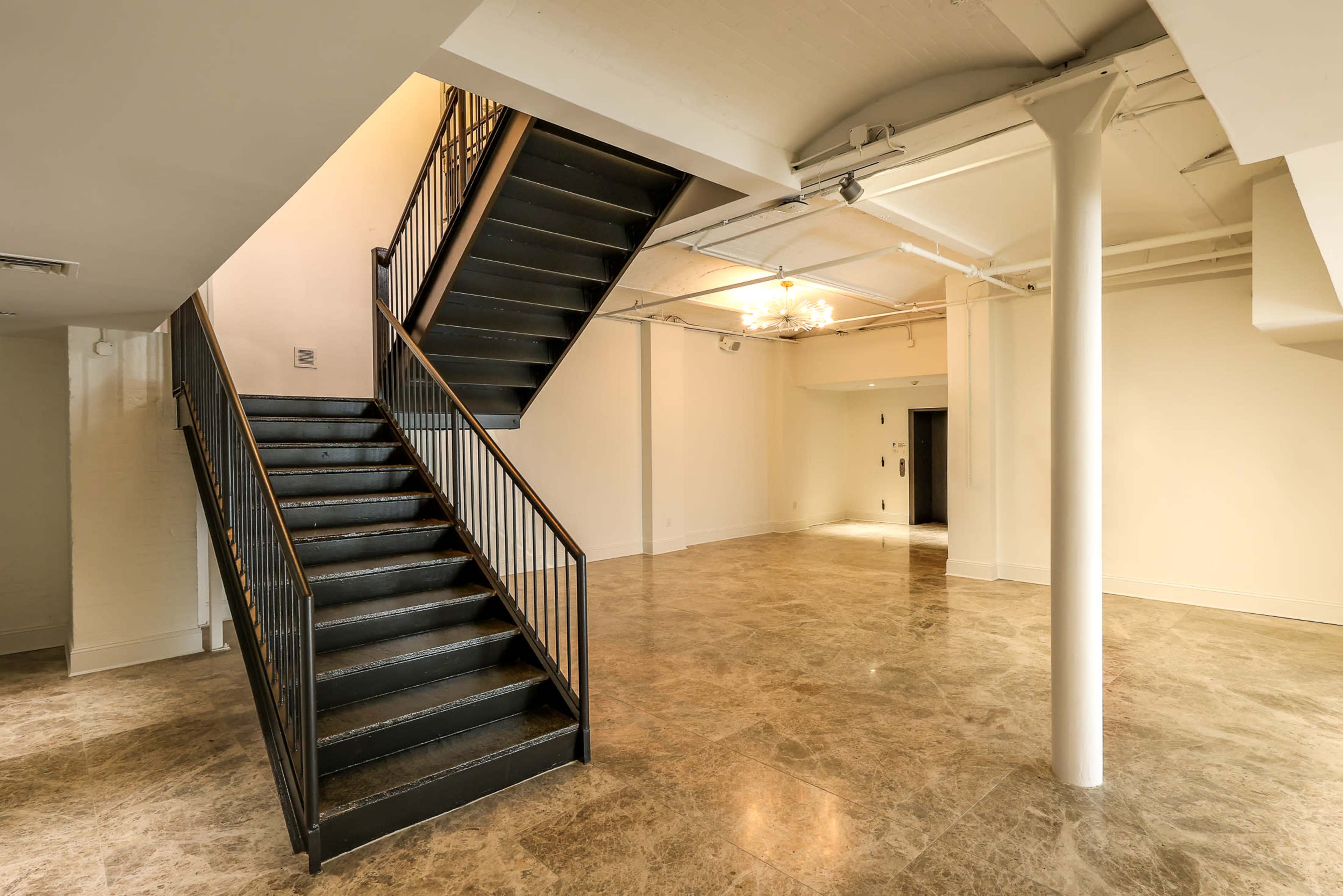 A spacious interior featuring a modern staircase, polished stone flooring, and a neutral color scheme with open walls.