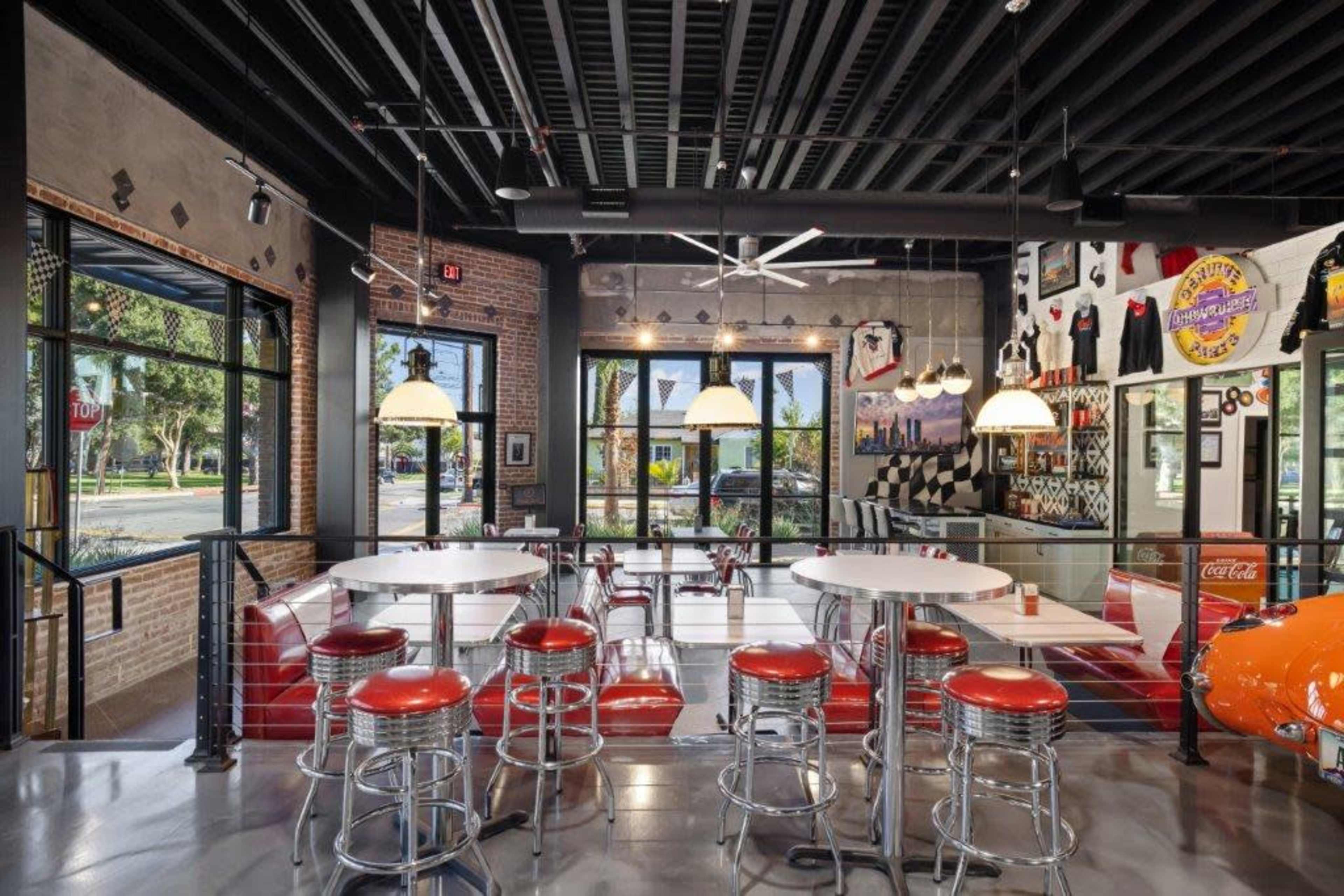 A modern diner interior featuring red bar stools, white tables, and large windows bringing in natural light.