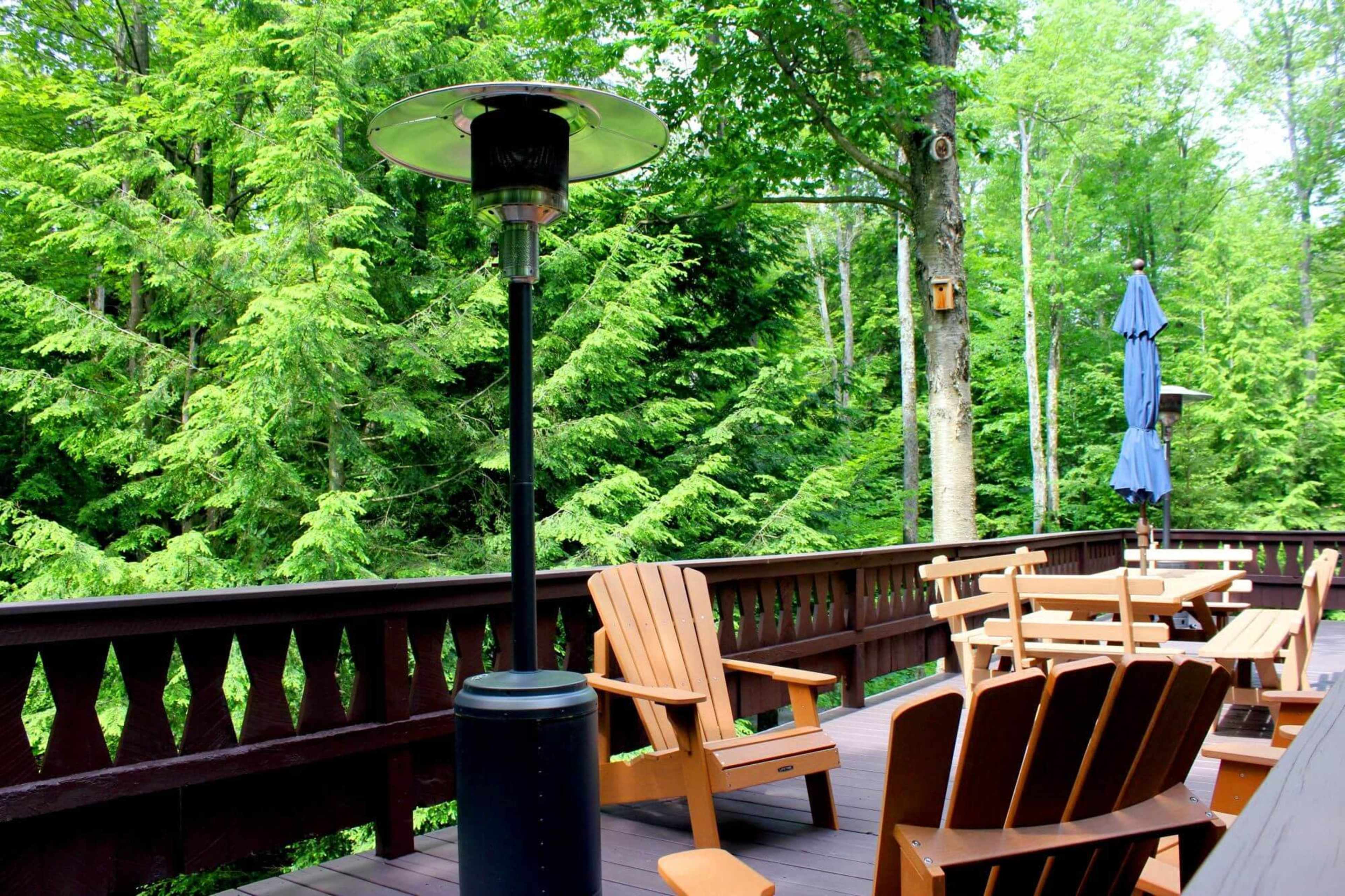 A deck area with wooden furniture and a patio heater overlooks a lush, green forest.