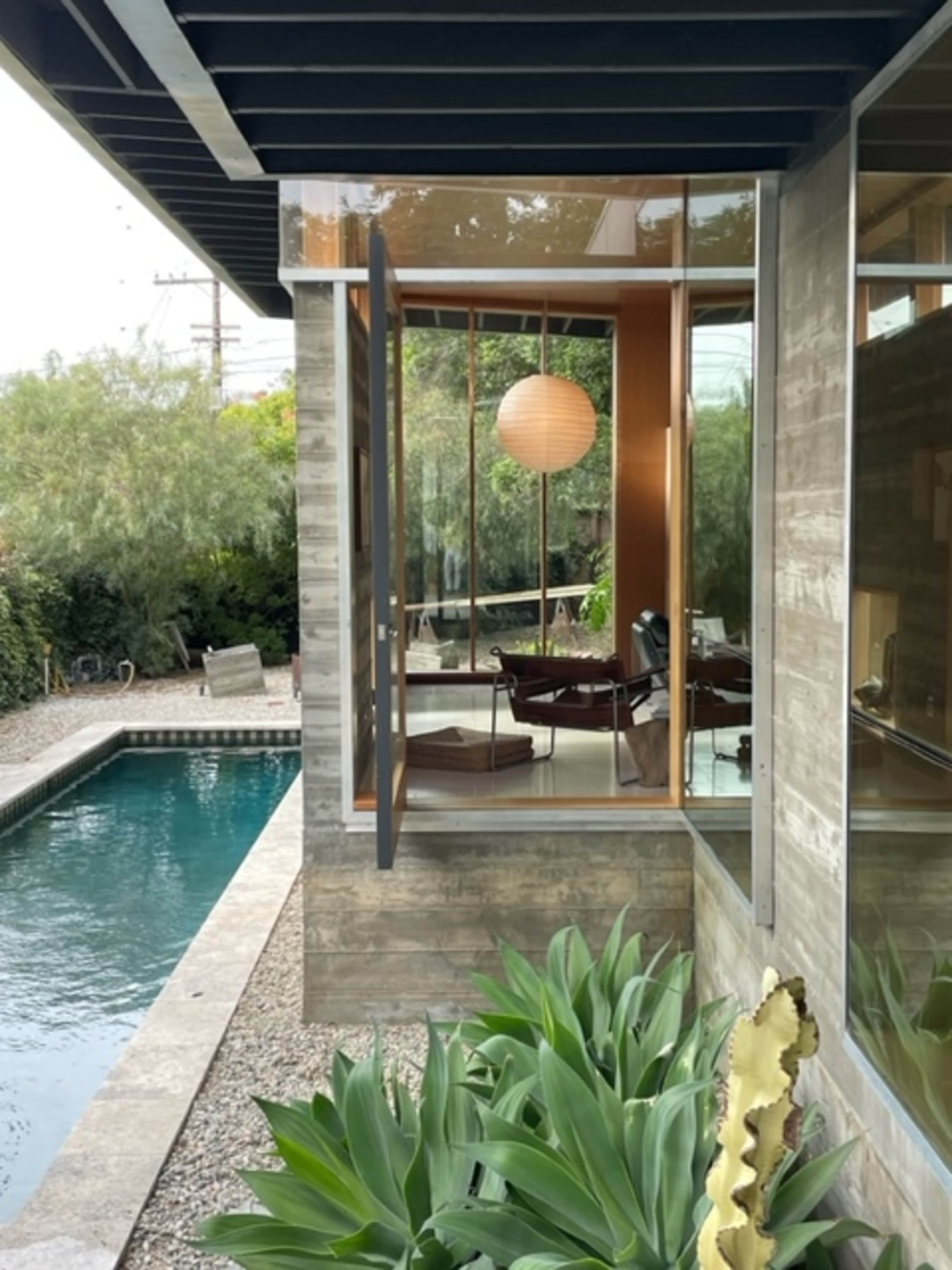 A modern home features large windows that open to a swimming pool surrounded by greenery.