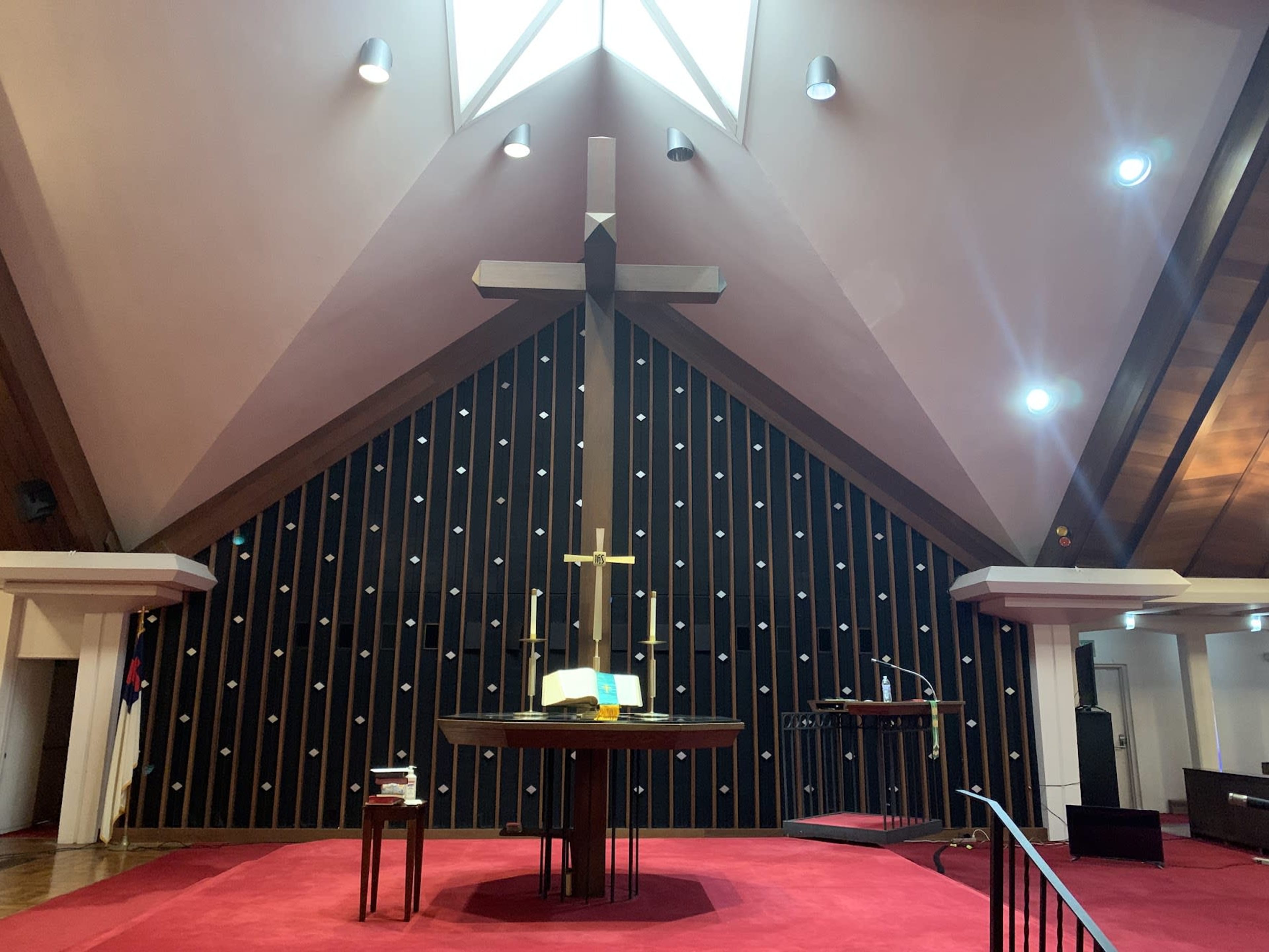 A modern church interior with a large wooden cross at the center, a circular altar, and a sloping ceiling.