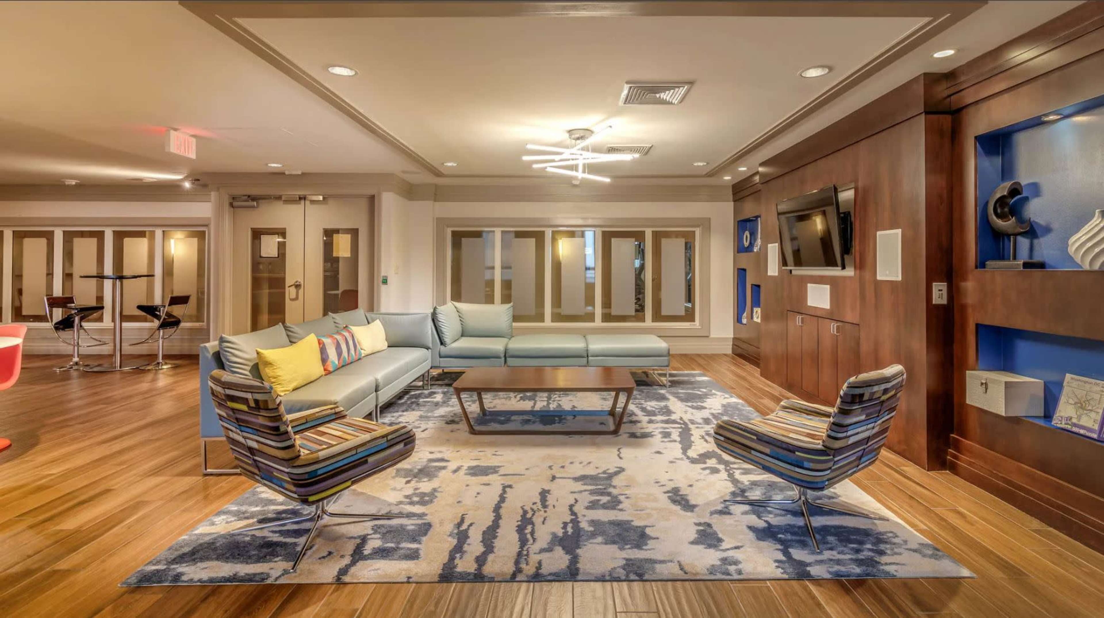 A modern lounge area featuring a sectional sofa, two striped chairs, a wooden coffee table, and a decorative rug on a hardwood floor.