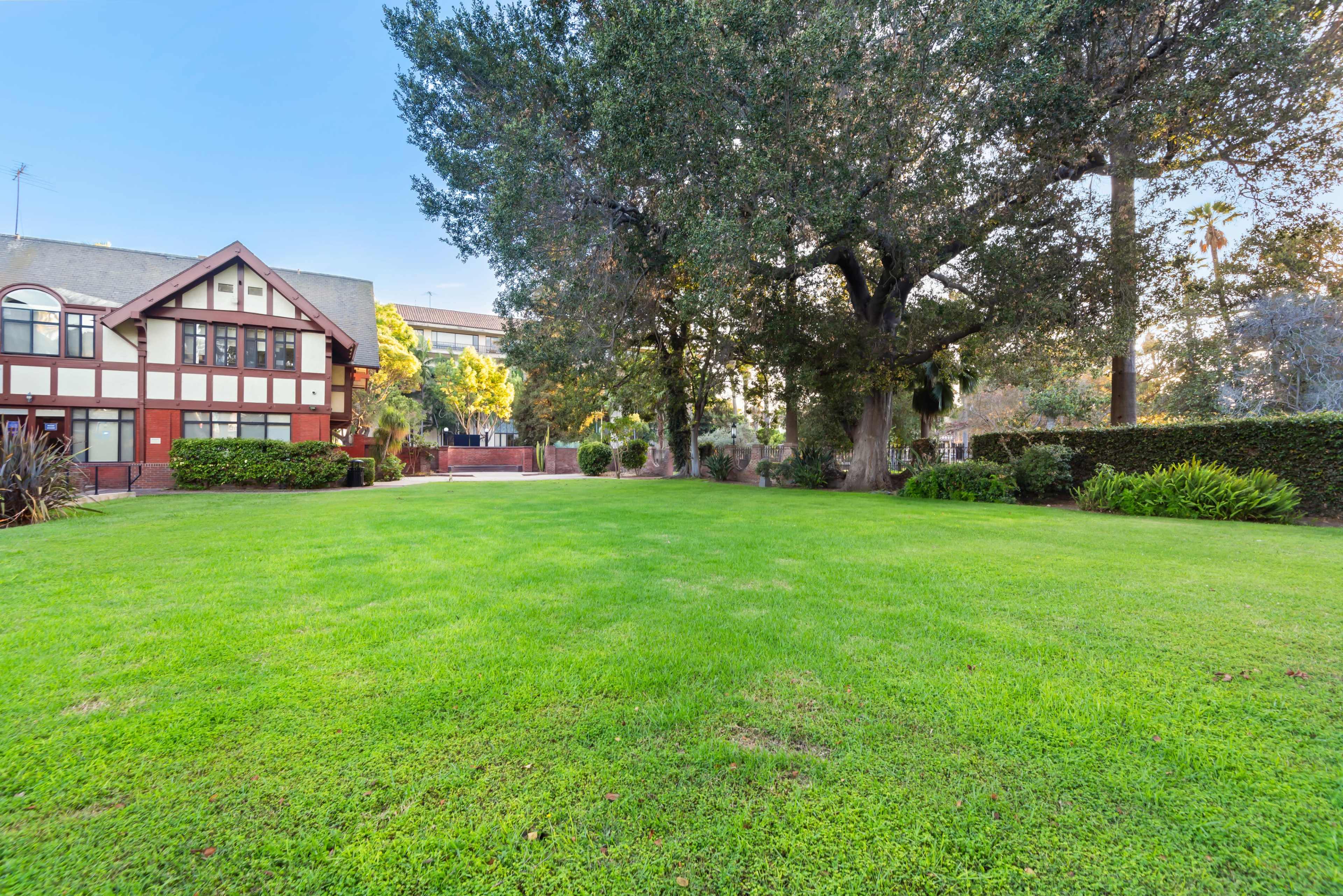 The image shows a well-maintained lawn in front of a large, two-story house surrounded by trees and shrubs.