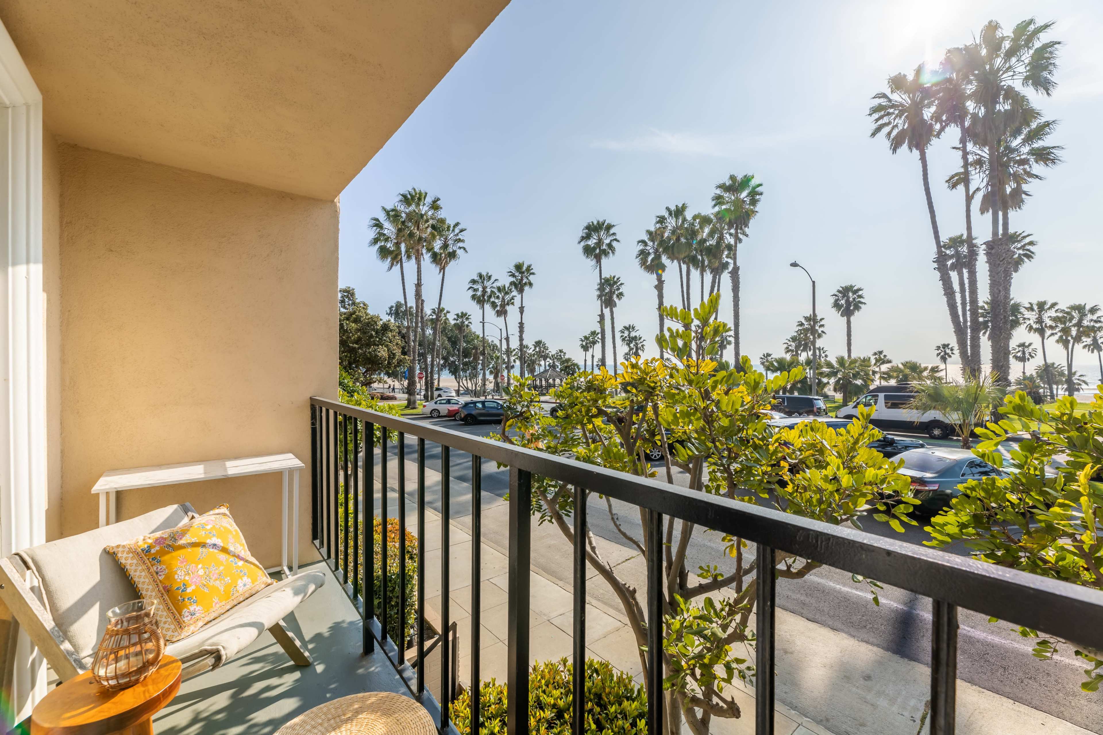 A balcony overlooks a street lined with palm trees and parked cars, with sunlight streaming in.