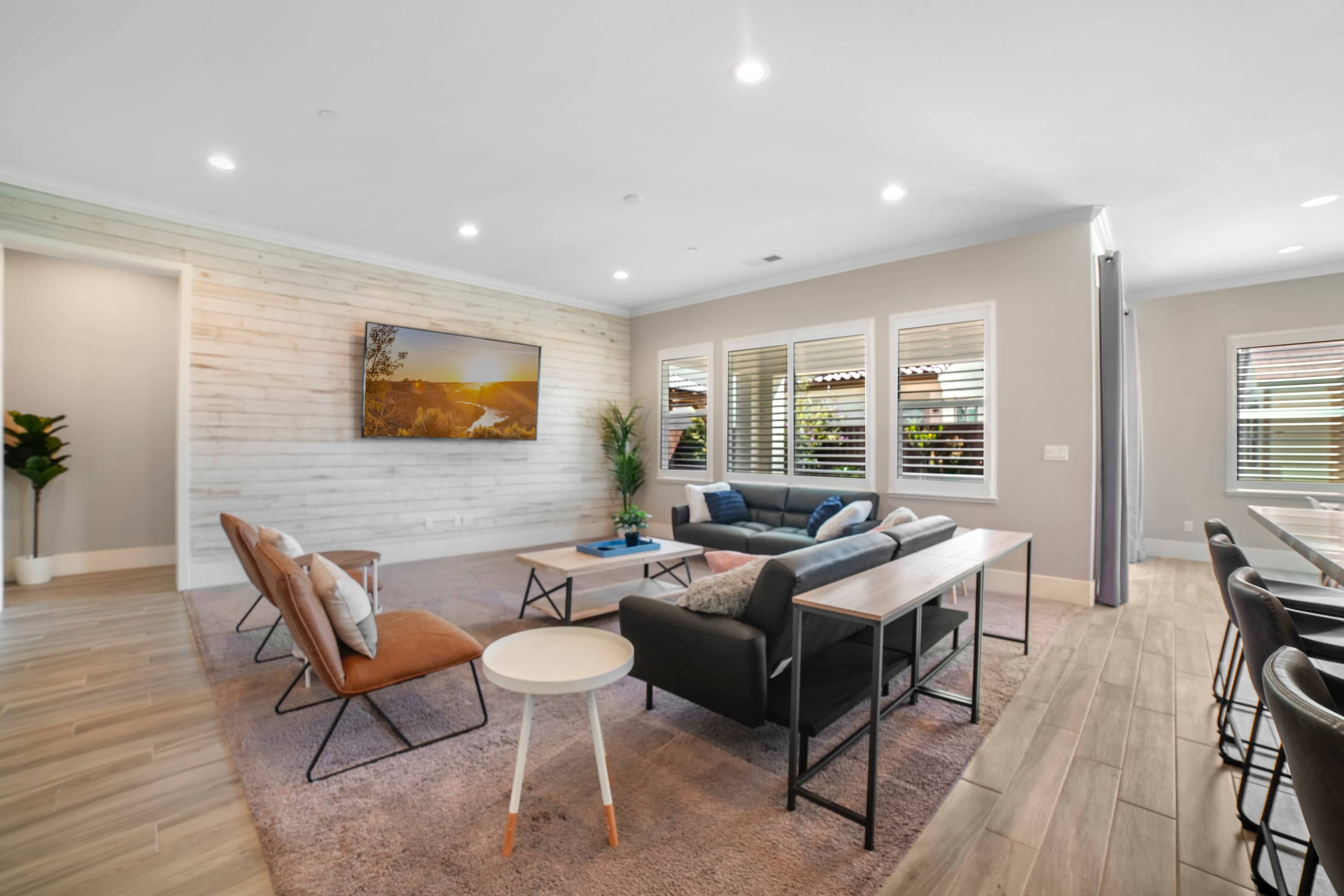 A modern living room featuring a combination of seating options, a wooden accent wall, and large windows with blinds.
