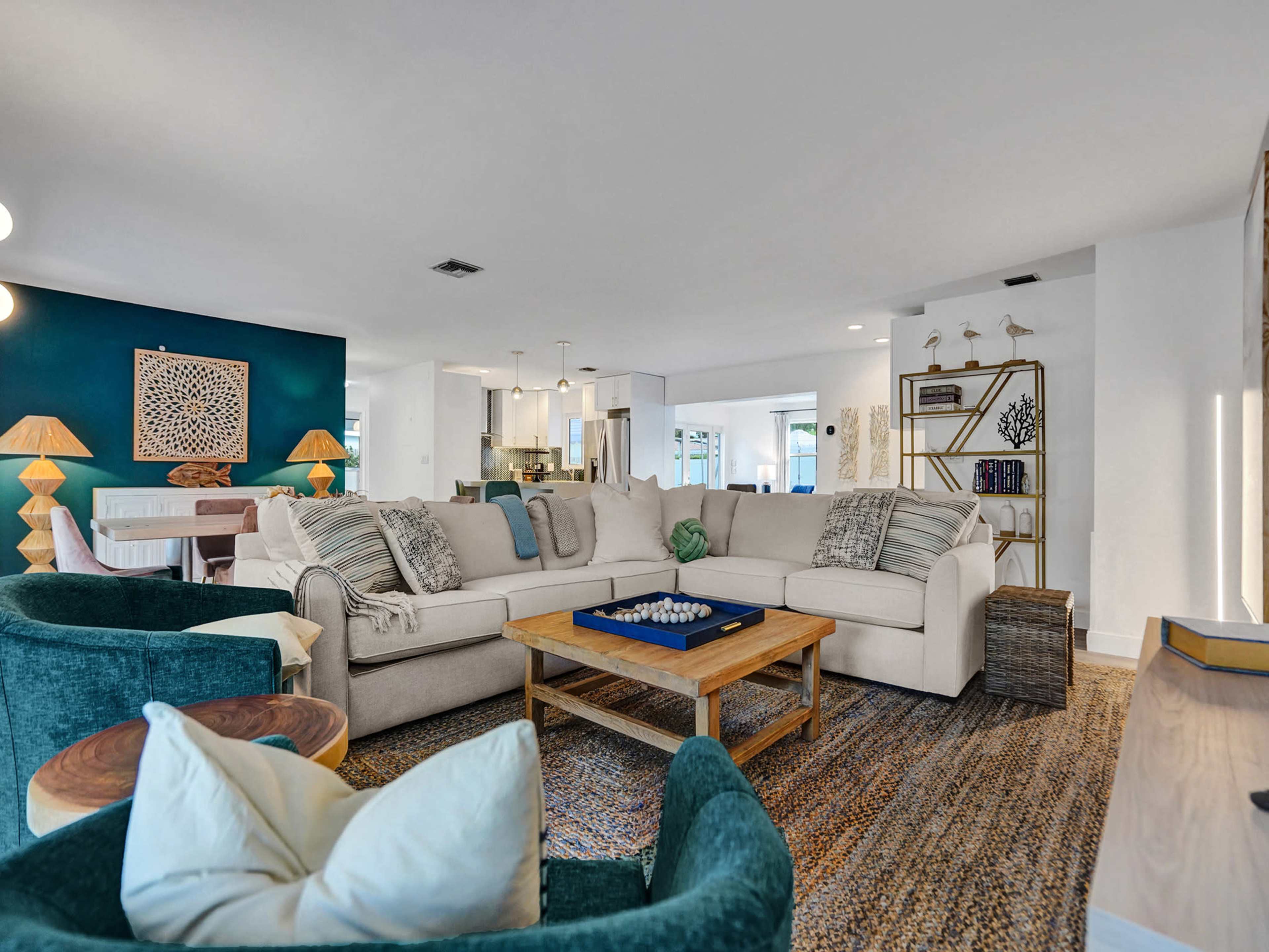 The spacious living room features a large sectional sofa, a wooden coffee table, and a mix of green chairs, with a dark accent wall and an open layout toward the kitchen.