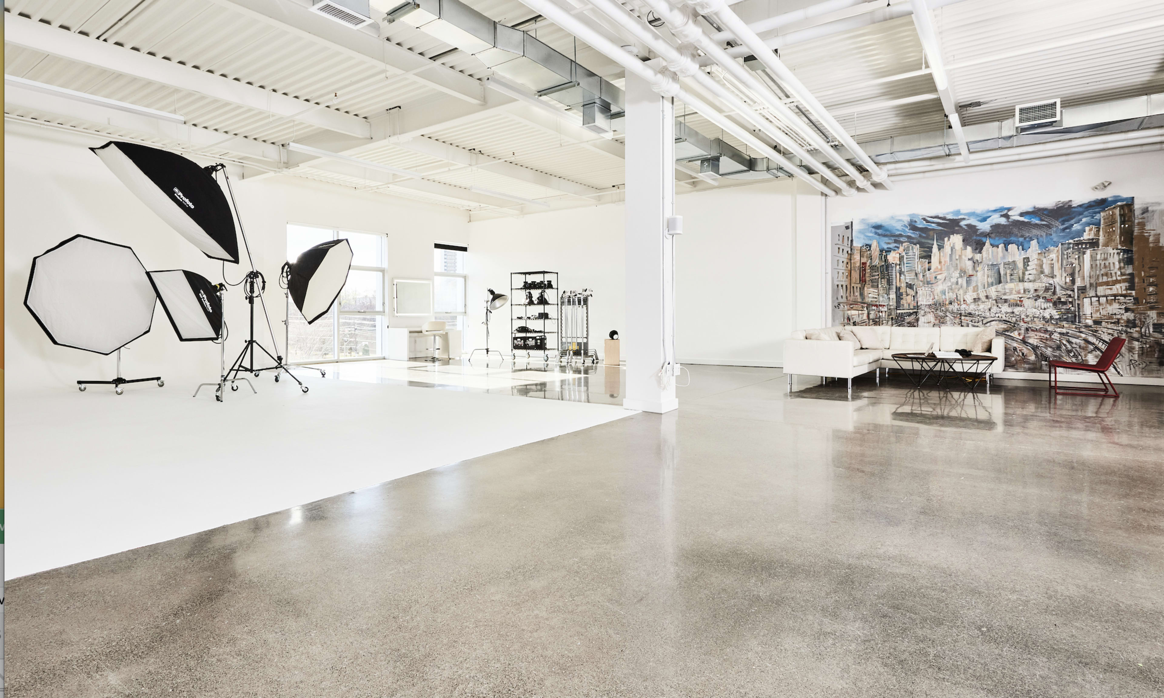 A spacious photography studio with various equipment, including softboxes and a backdrop, alongside modern furniture.