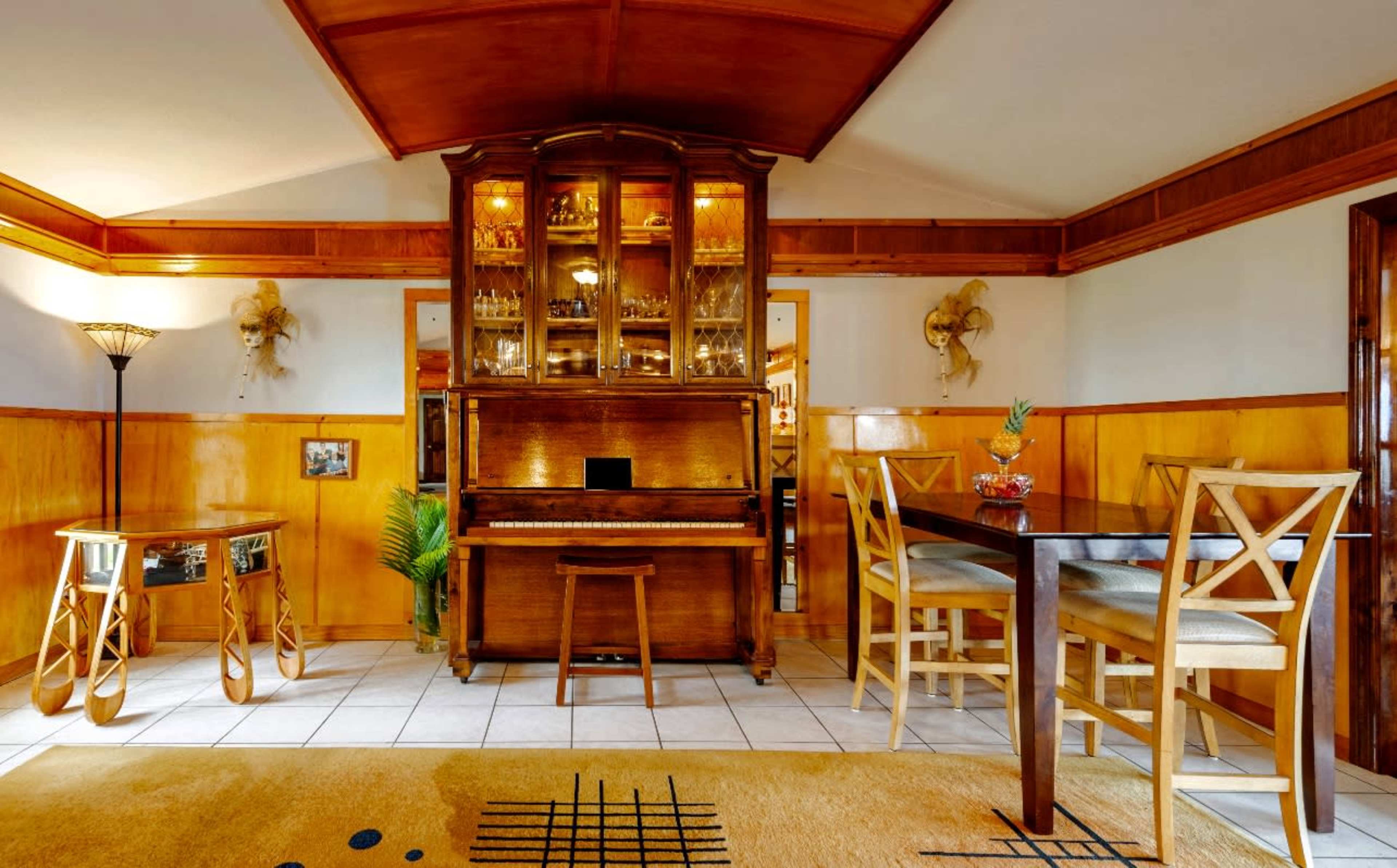 A room with wooden walls, a vintage piano, a dining table, and decorative elements including plants and wall art.