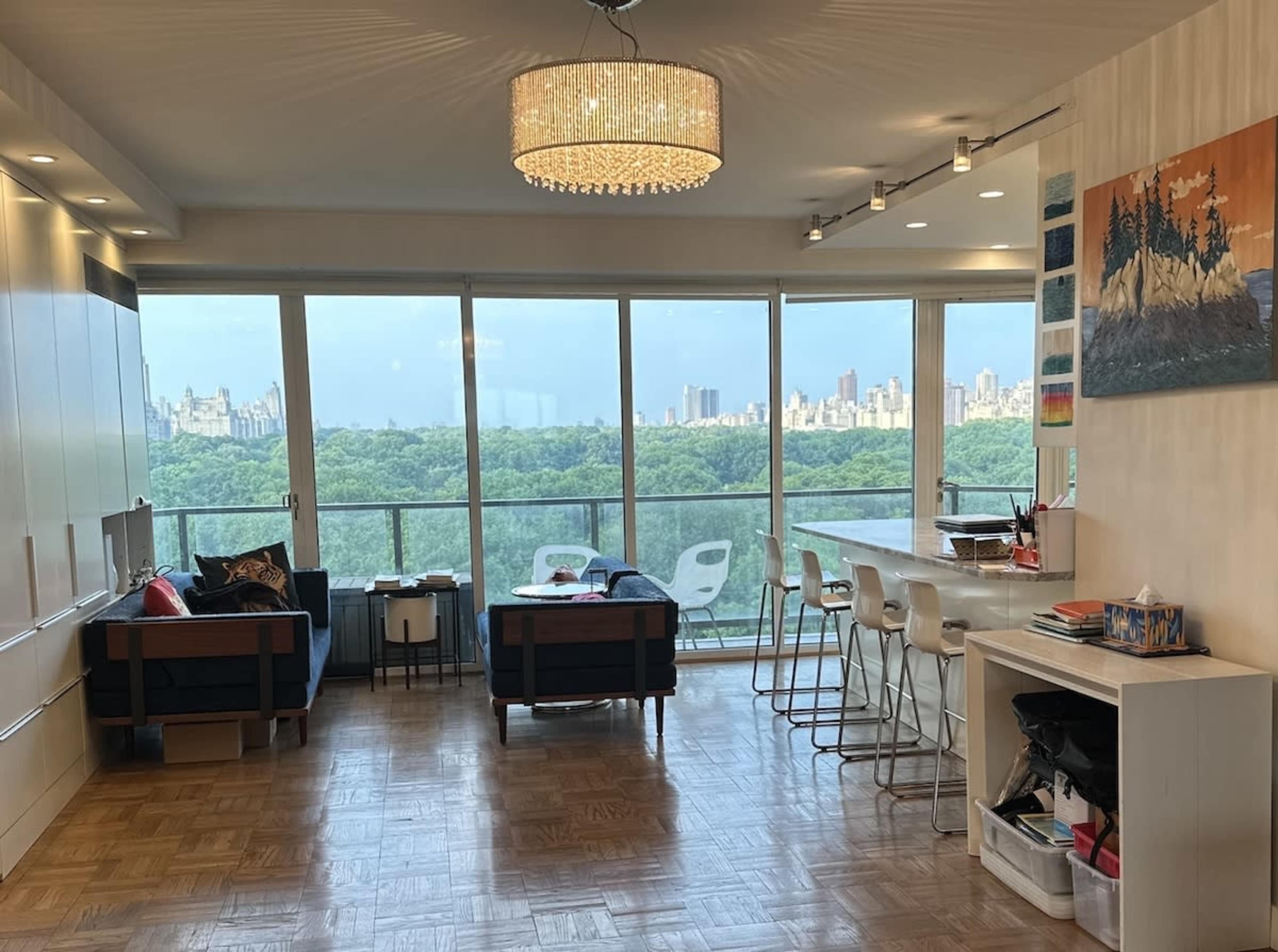 A modern apartment features a spacious living area with large windows overlooking a green landscape and city skyline.