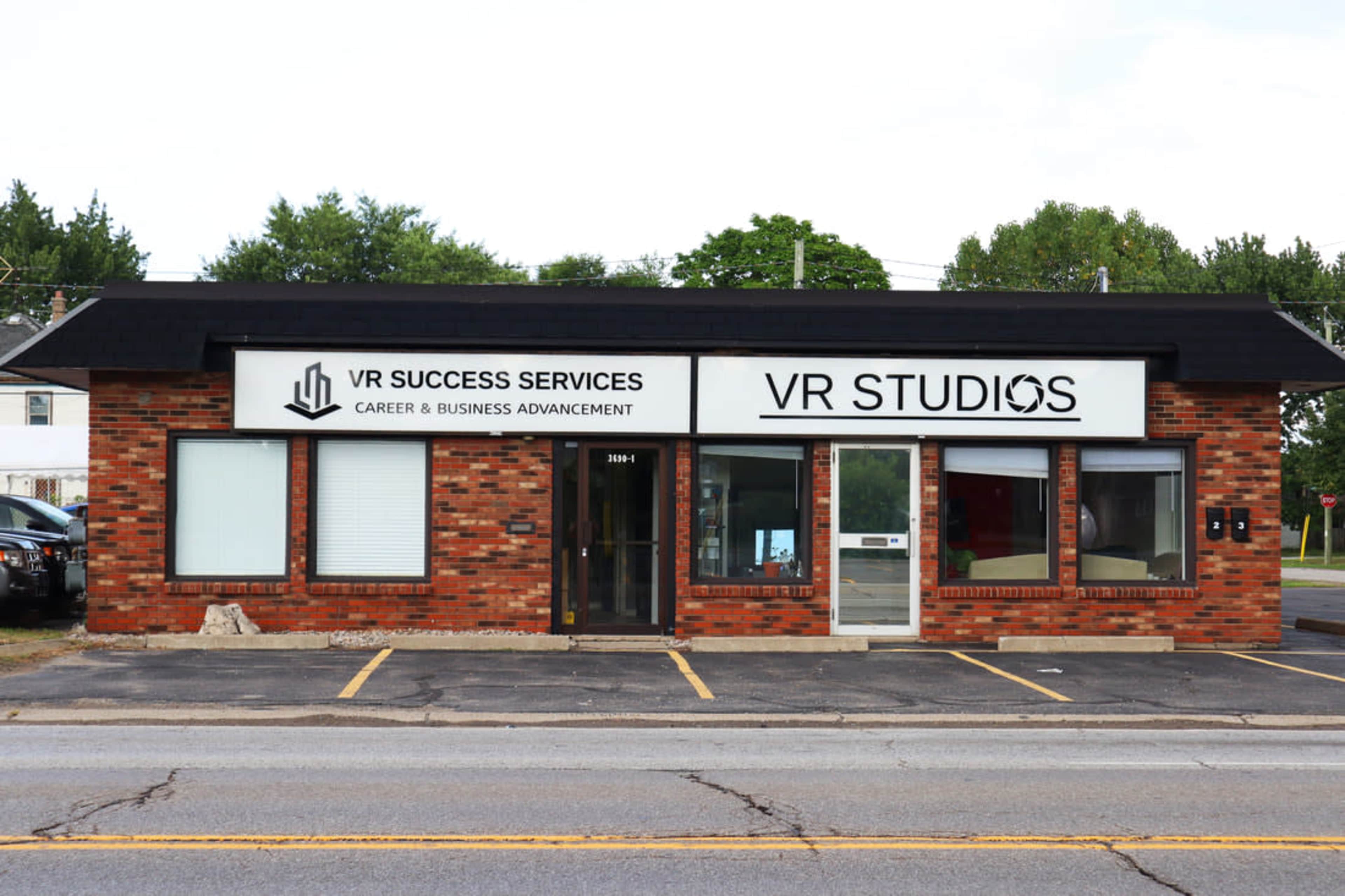 A brick building displays the signs for "VR Success Services" and "VR Studios" across its facade, facing a street.