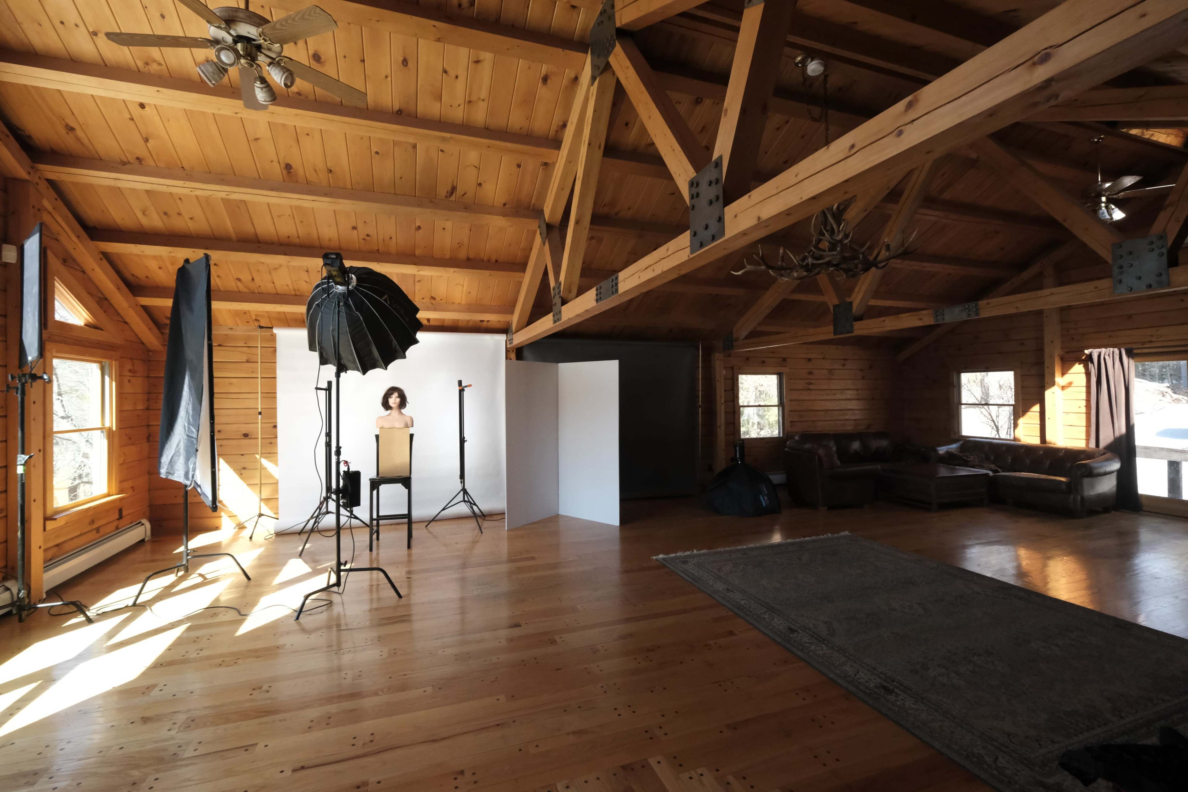 A spacious wooden interior with photography equipment, including softboxes and a backdrop, set up for a photoshoot.
