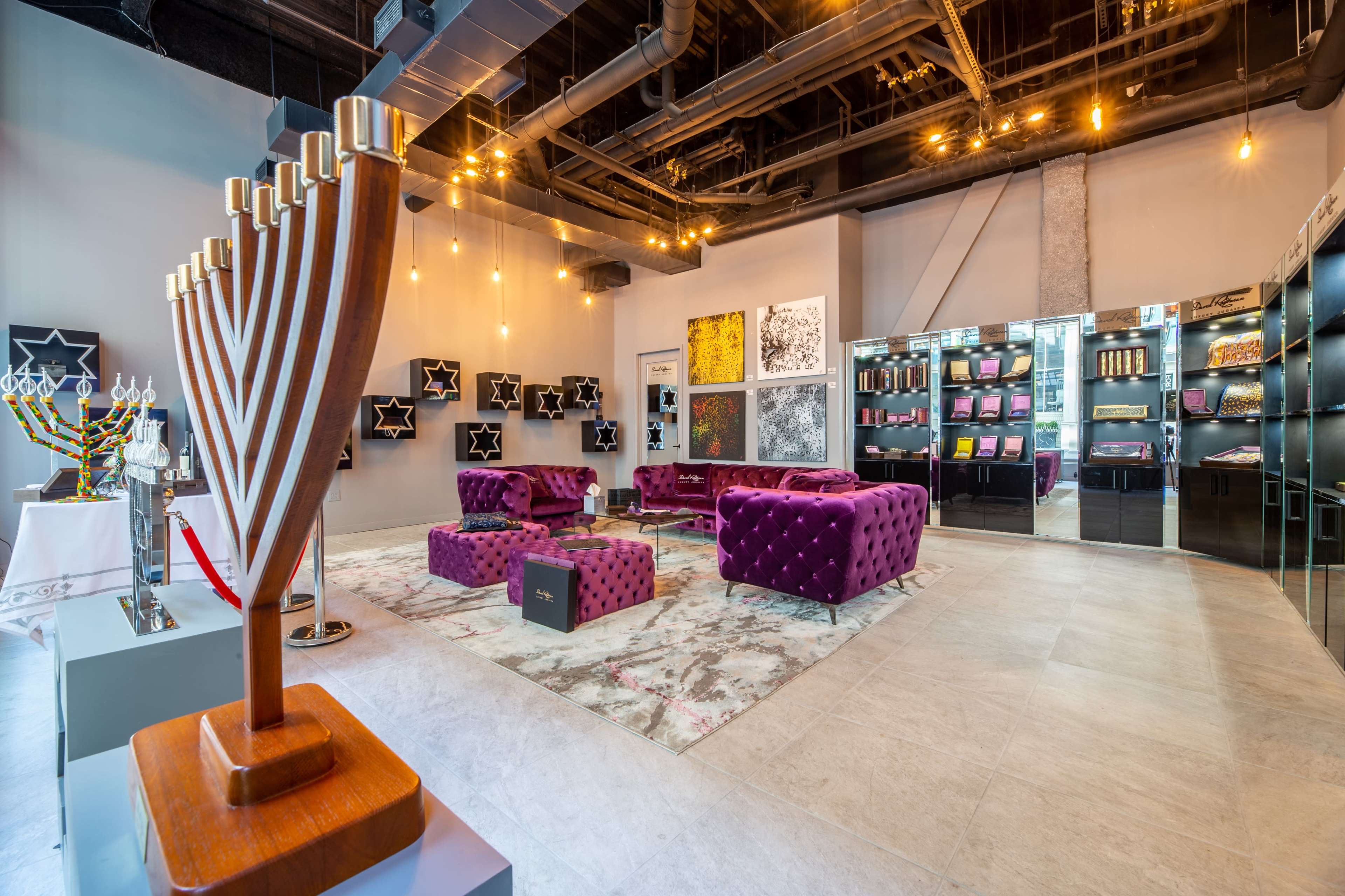 The image shows a modern retail space featuring plush purple seating, a decorative menorah, and various artistic displays on the walls.