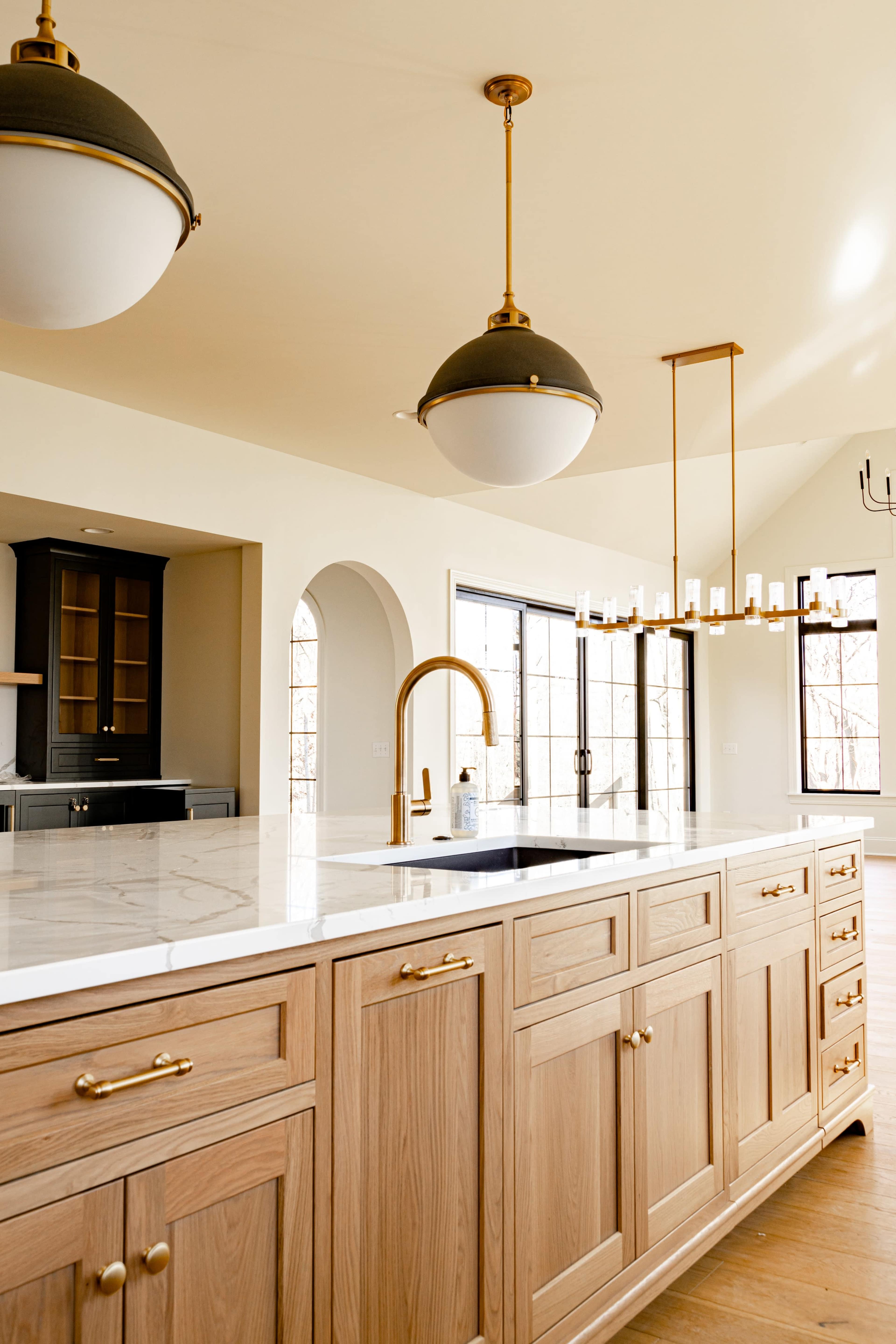 The image shows a kitchen with wooden cabinetry, a marble countertop, and stylish pendant lighting.
