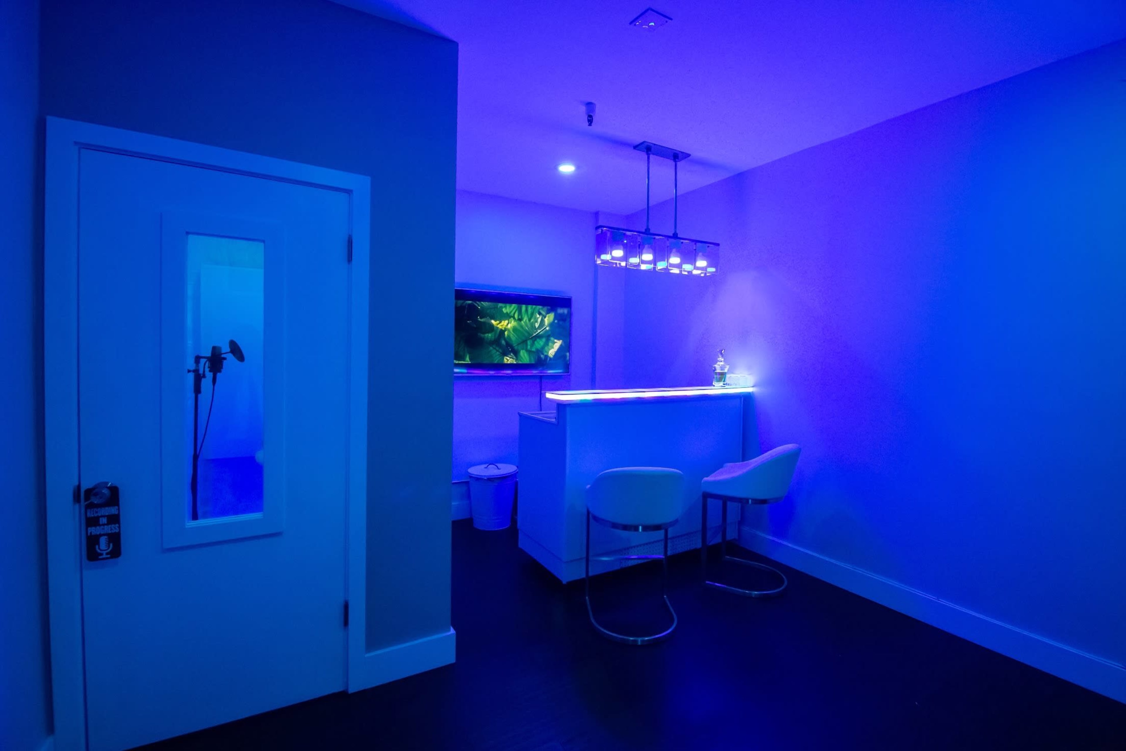 A dimly lit room features a small bar with bar stools, an aquarium on the wall, and a door with a glass panel.