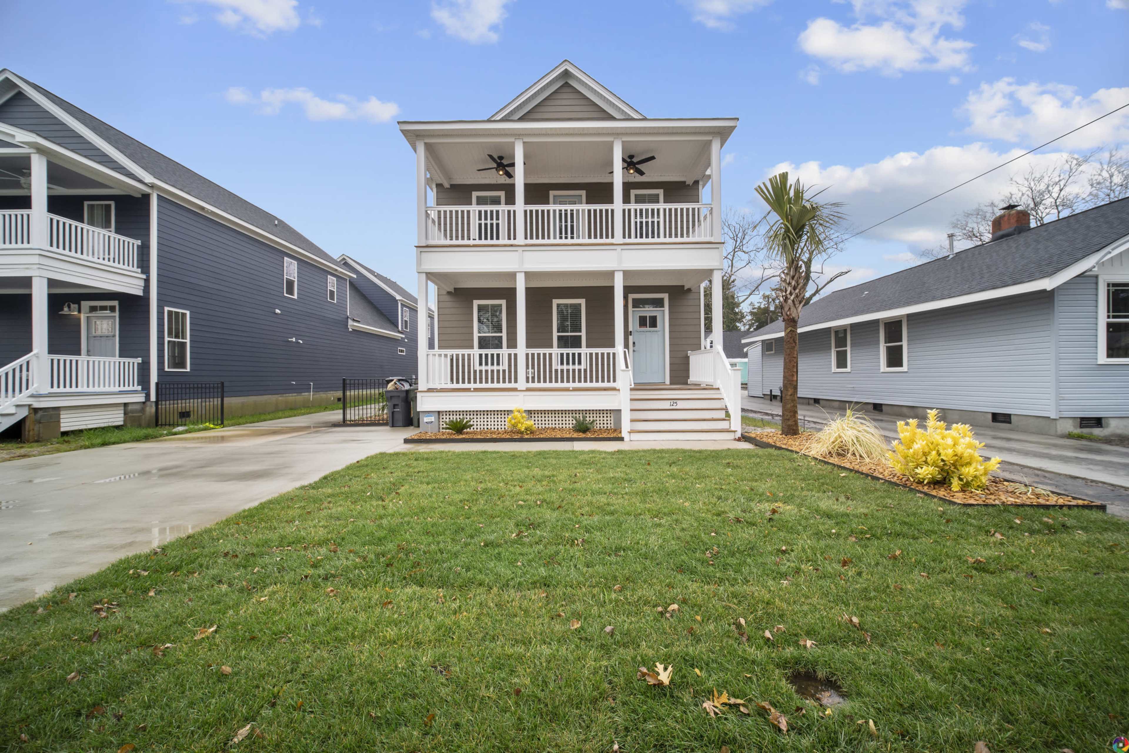 A two-story house with a porch, surrounded by a lawn featuring small shrubs and a palm tree.