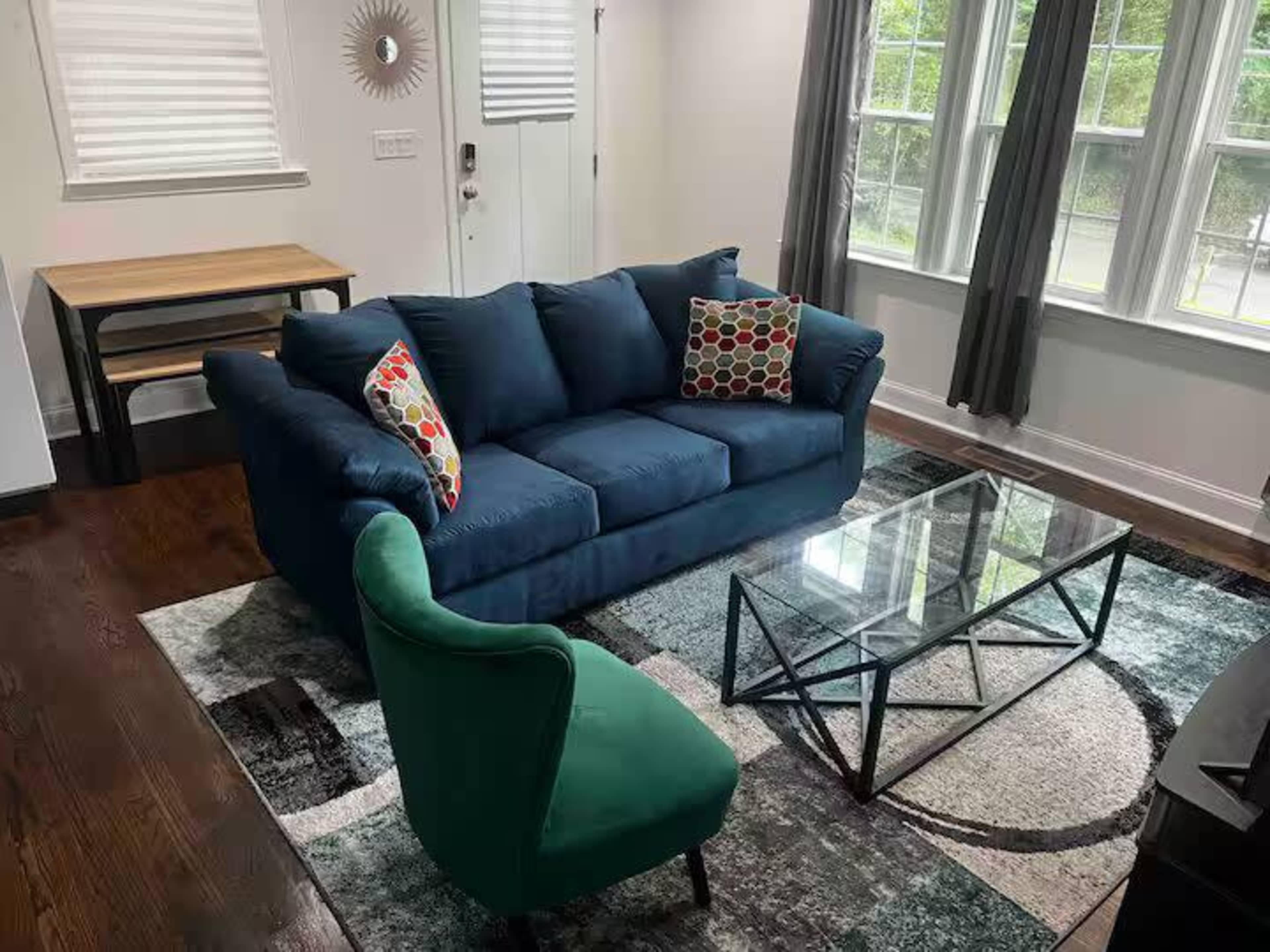 The image shows a living room with a blue sofa, a green armchair, a glass coffee table, and a wooden dining table in the background.