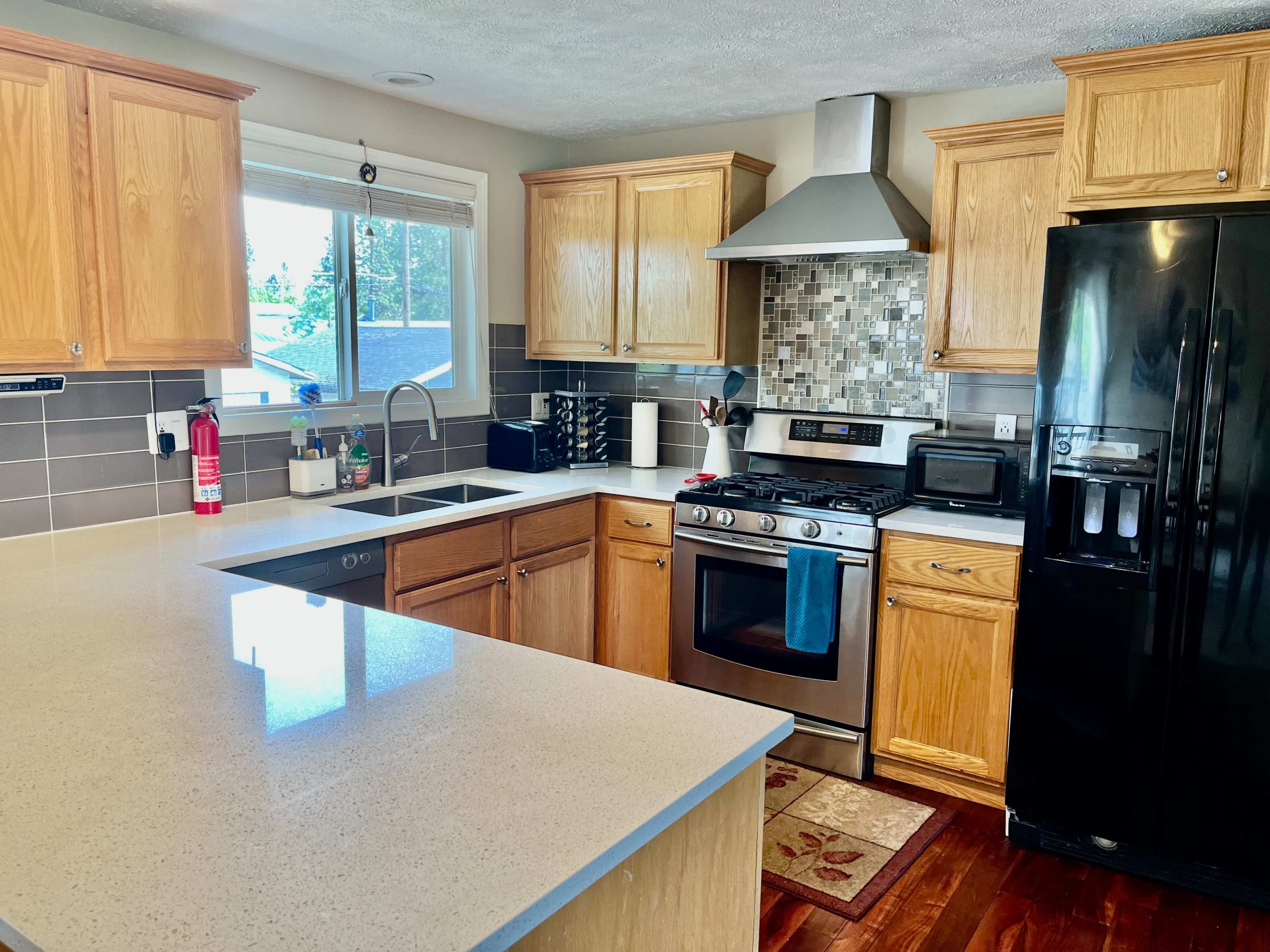 A modern kitchen features wooden cabinets, a stainless steel stove, a black refrigerator, and a countertop with a sink under a window.