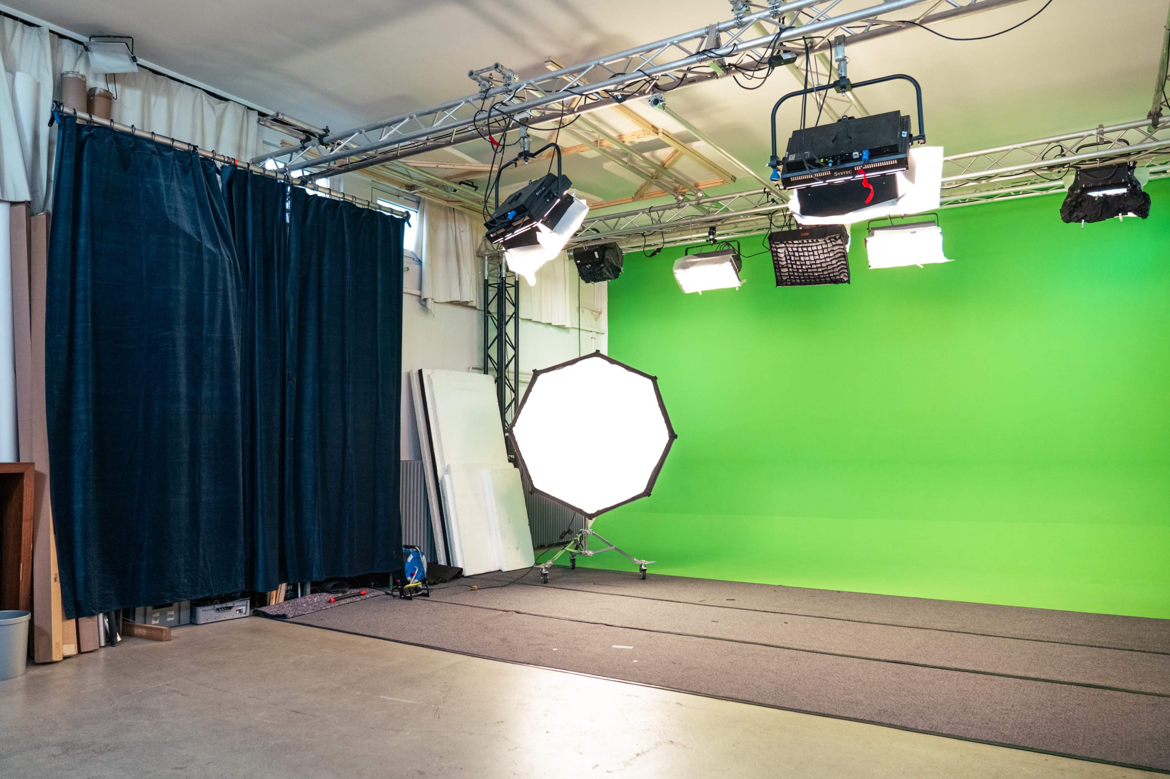 The image shows a photography studio with a green screen backdrop, studio lights, and a designated area for shooting.