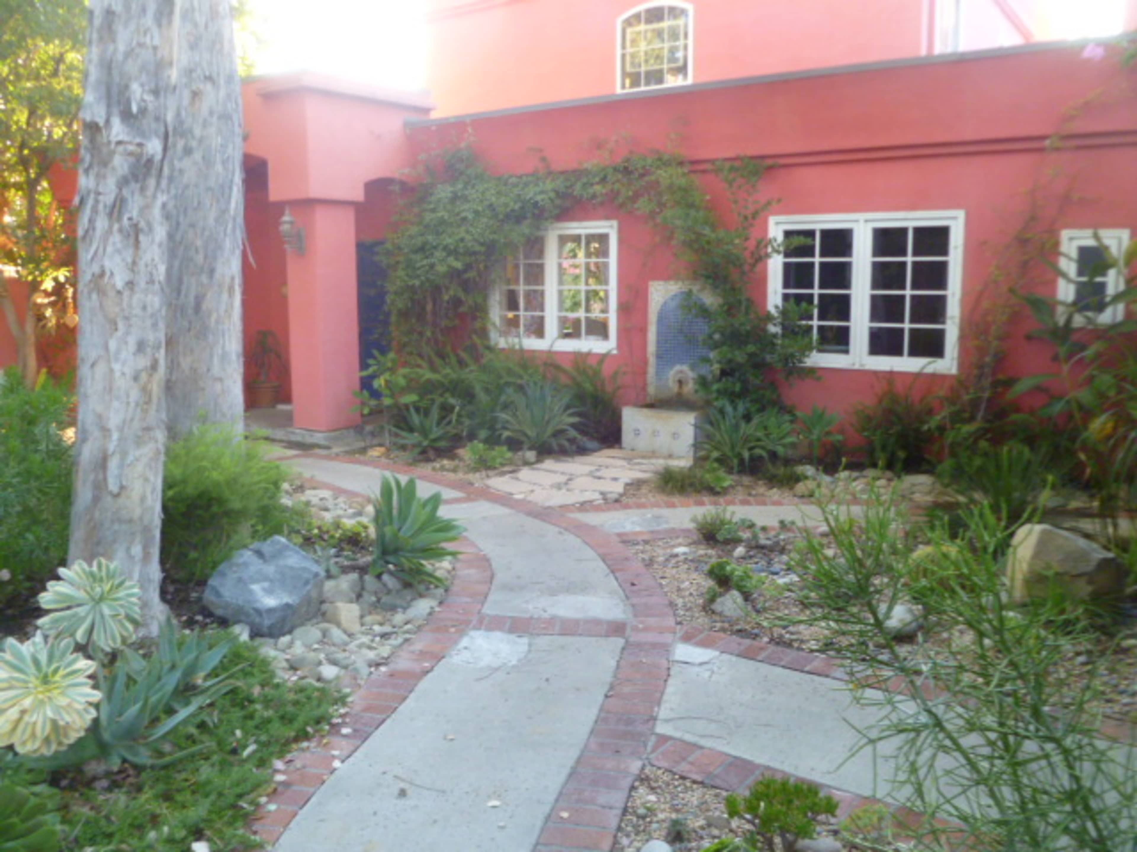 A landscaped pathway leading to a house with a pink exterior and several surrounding plants.