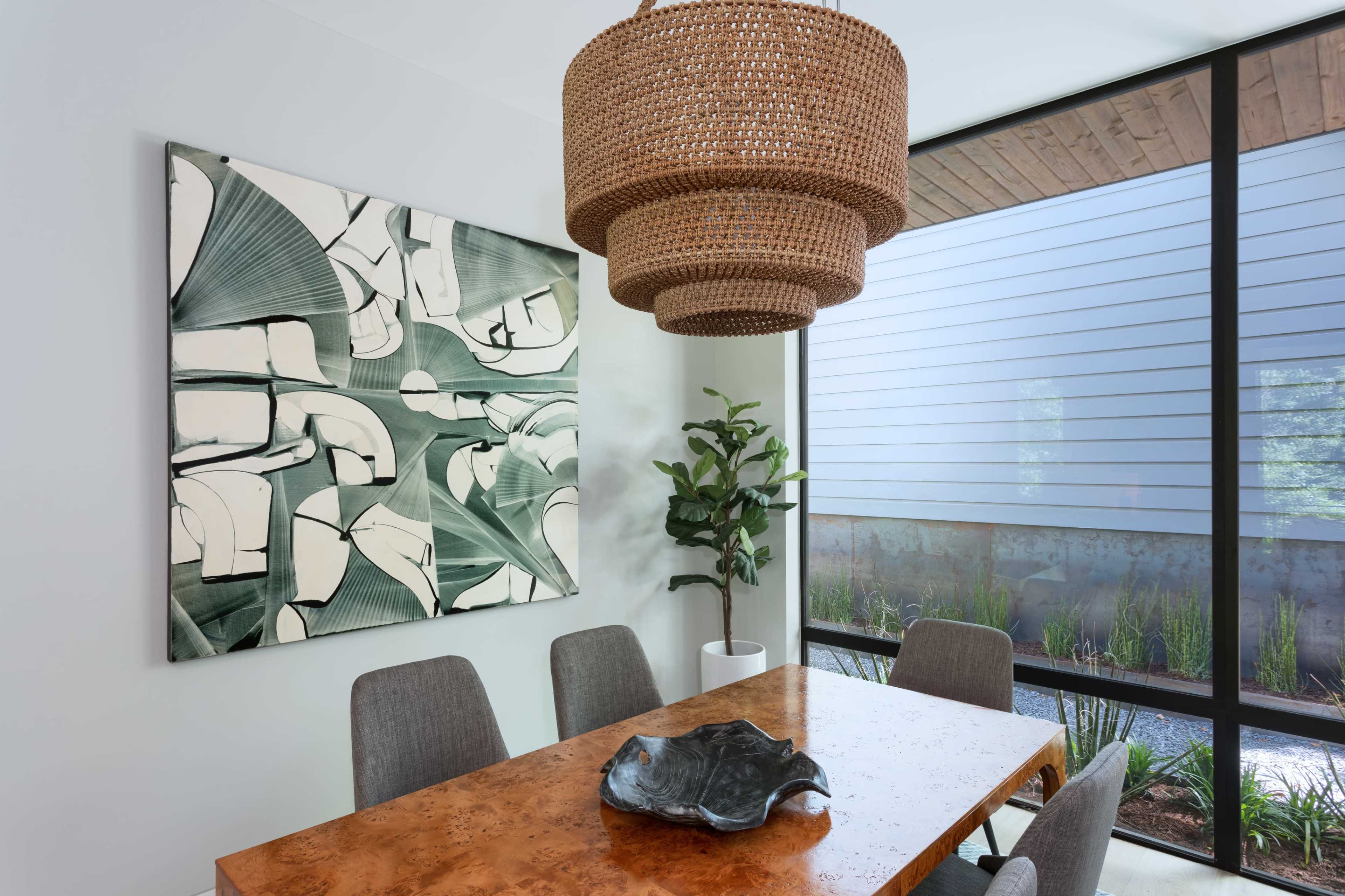 A dining area features a wooden table with gray chairs, a large woven pendant light, and a modern artwork hanging on the wall.