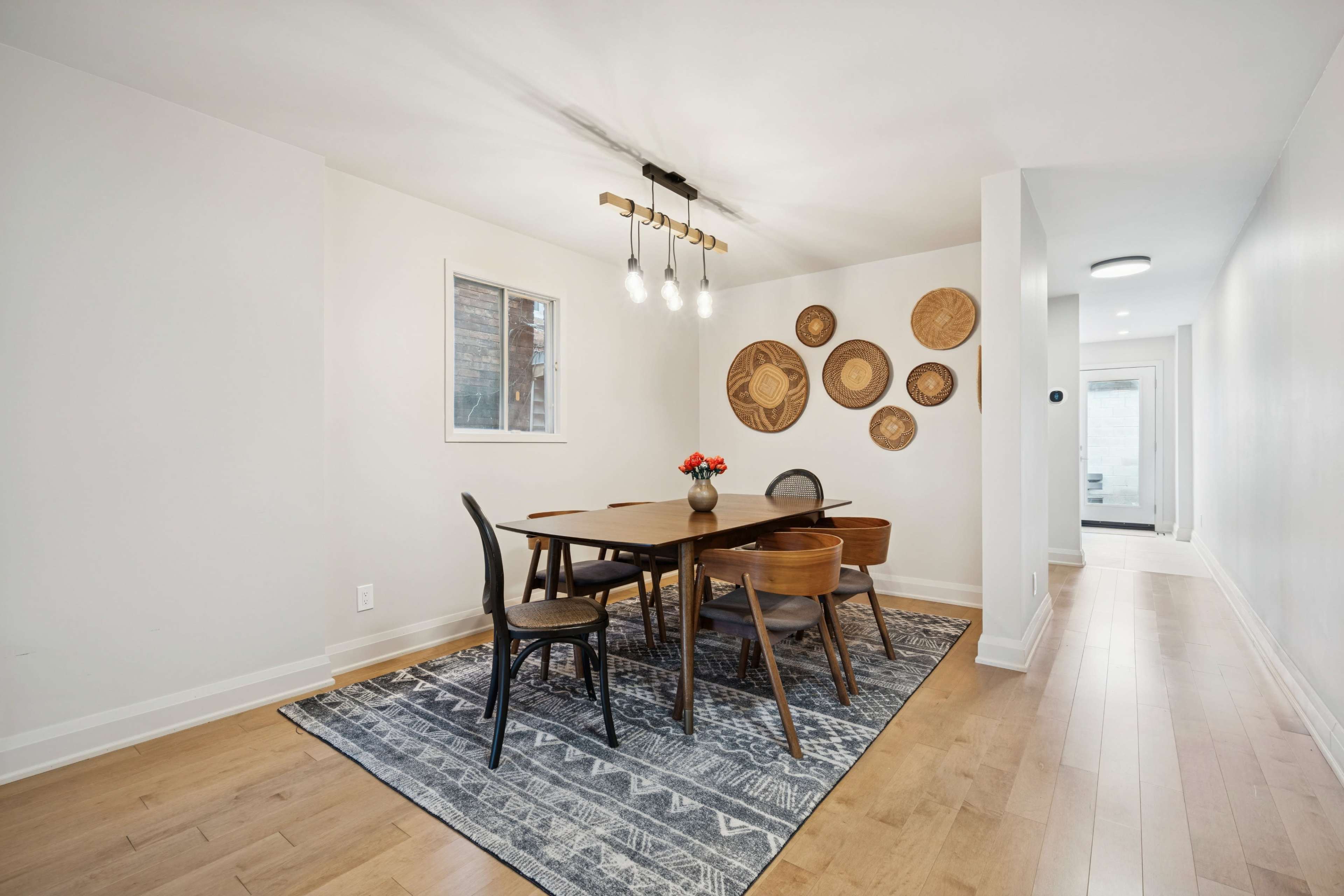 A dining area features a wooden table surrounded by chairs, with decorative wall plates and a light fixture overhead.