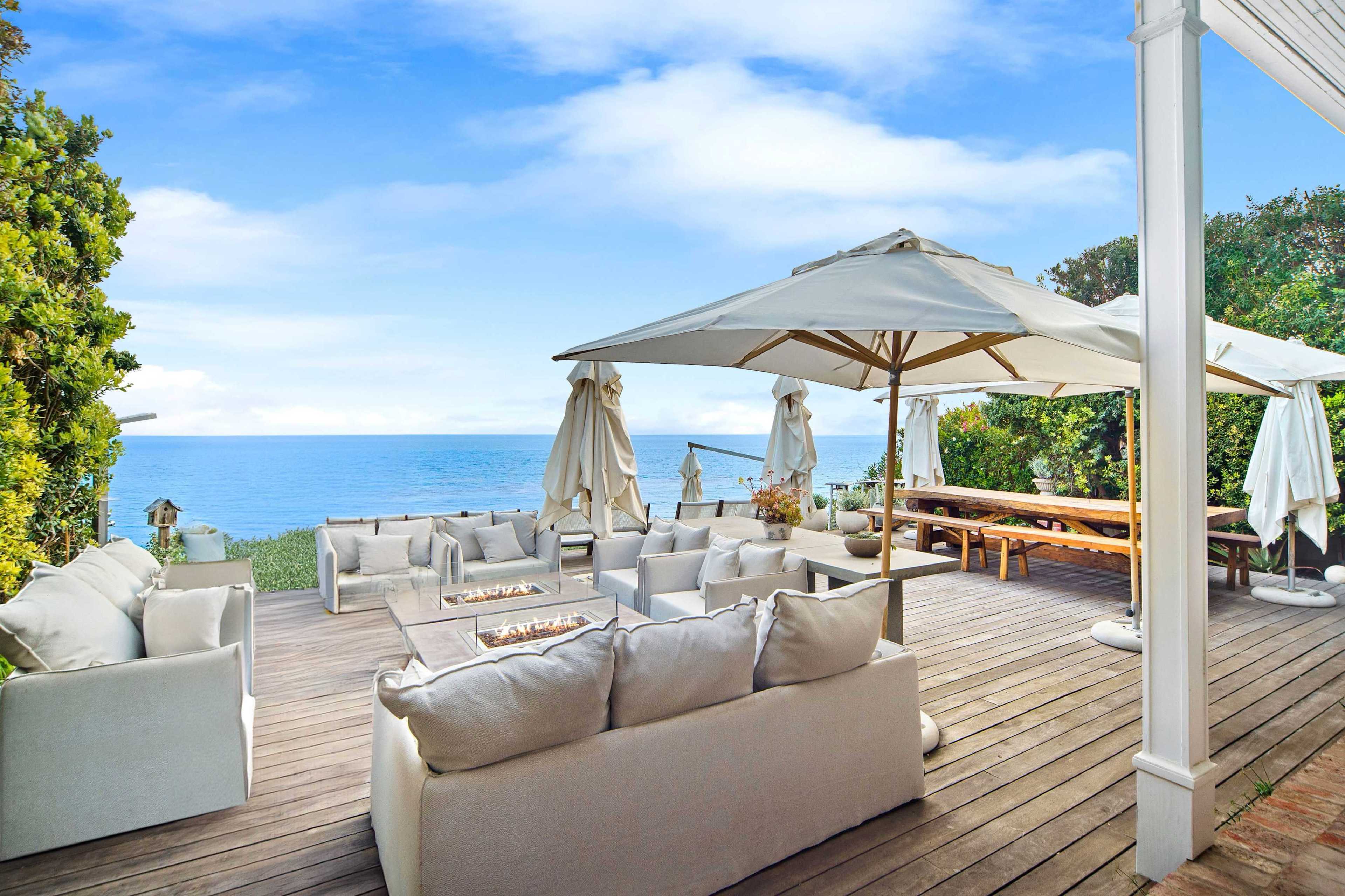 A spacious outdoor patio features comfortable seating arrangements and umbrellas overlooking the ocean.