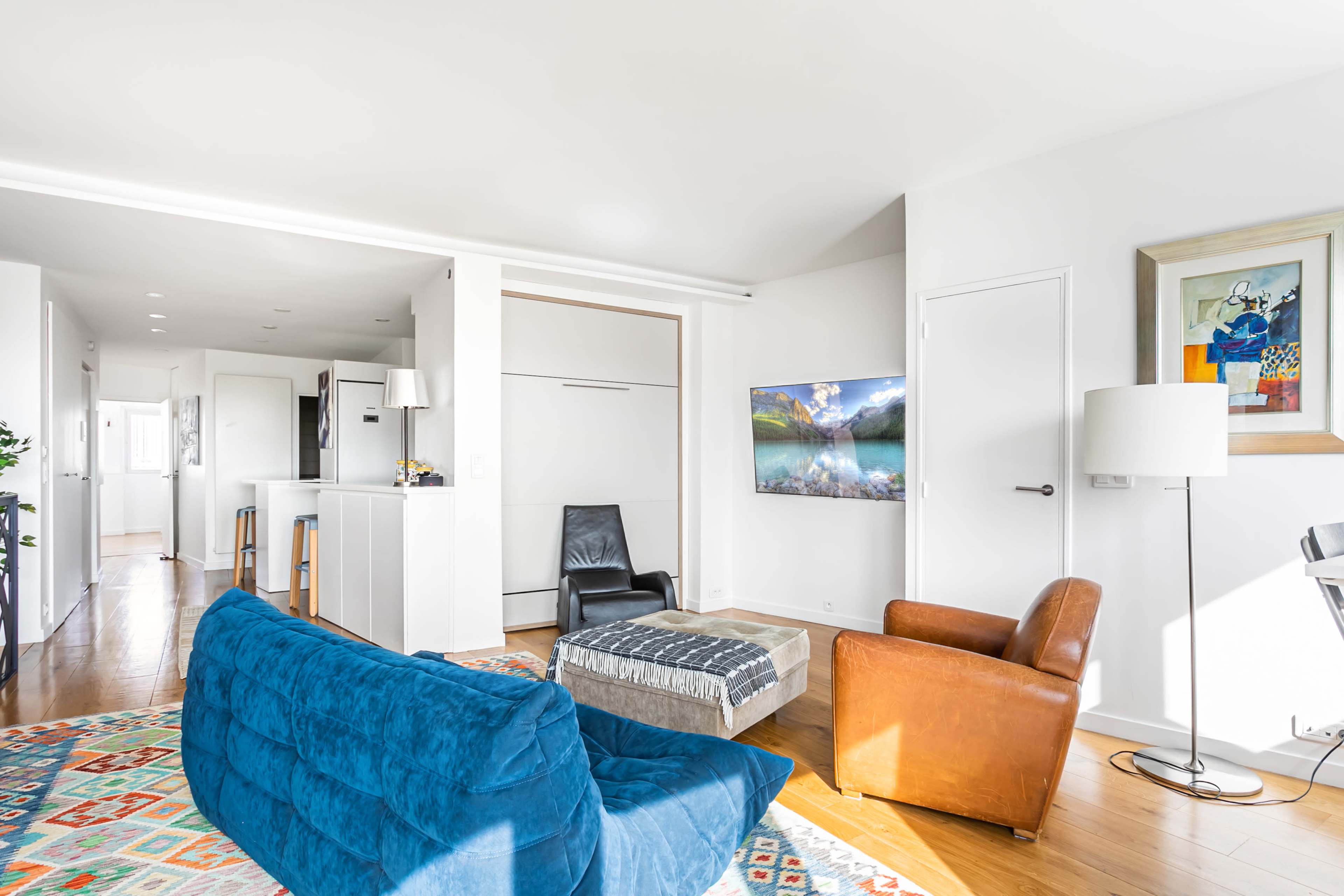 A modern living space features a blue sofa, a brown armchair, a coffee table, and a wall-mounted TV.