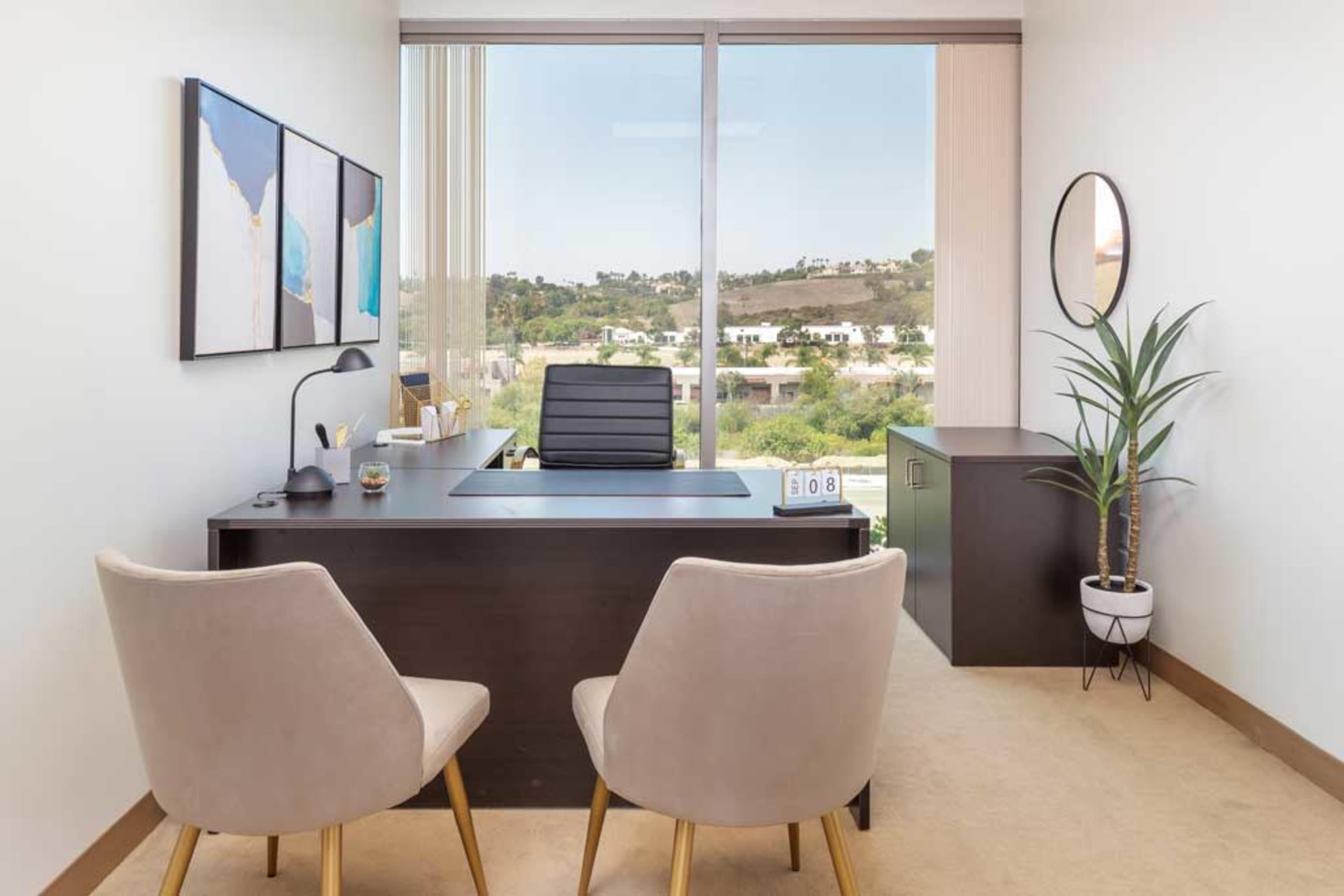 The image shows a modern office space with a dark desk, two light-colored chairs, and a large window overlooking a green landscape.