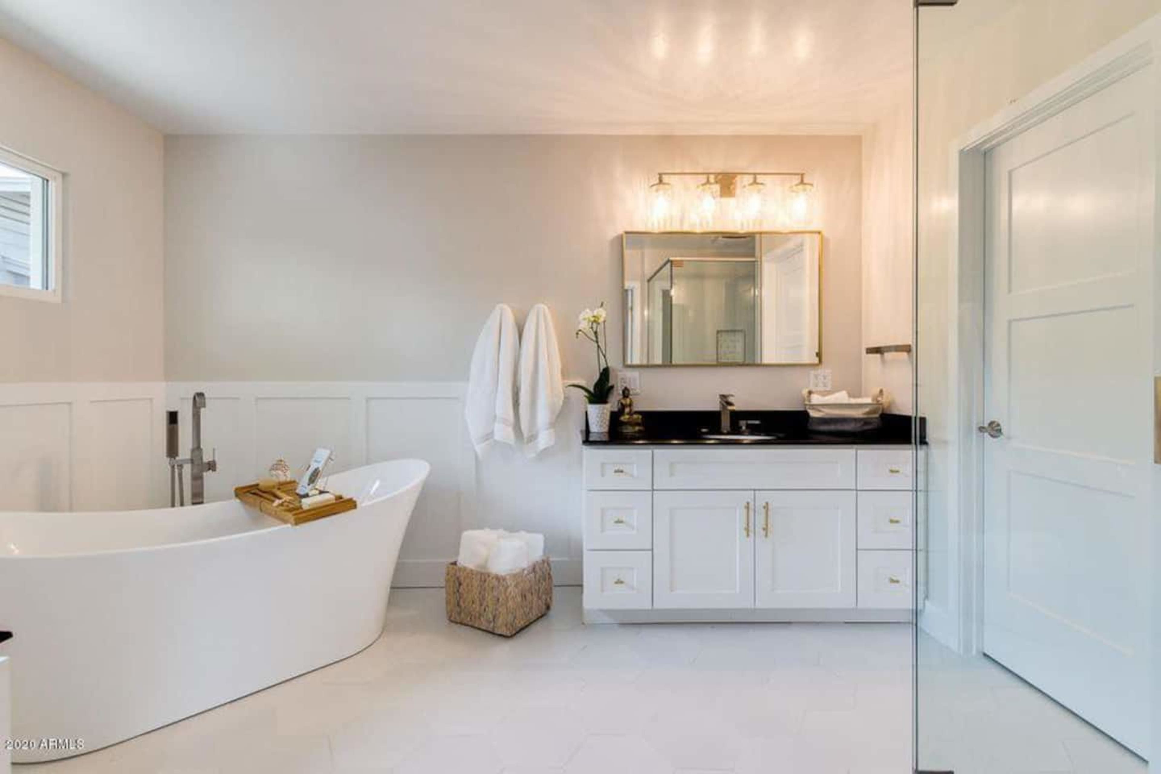A clean, modern bathroom features a freestanding bathtub, a double-sink vanity with a black countertop, and white cabinetry against light-colored walls.