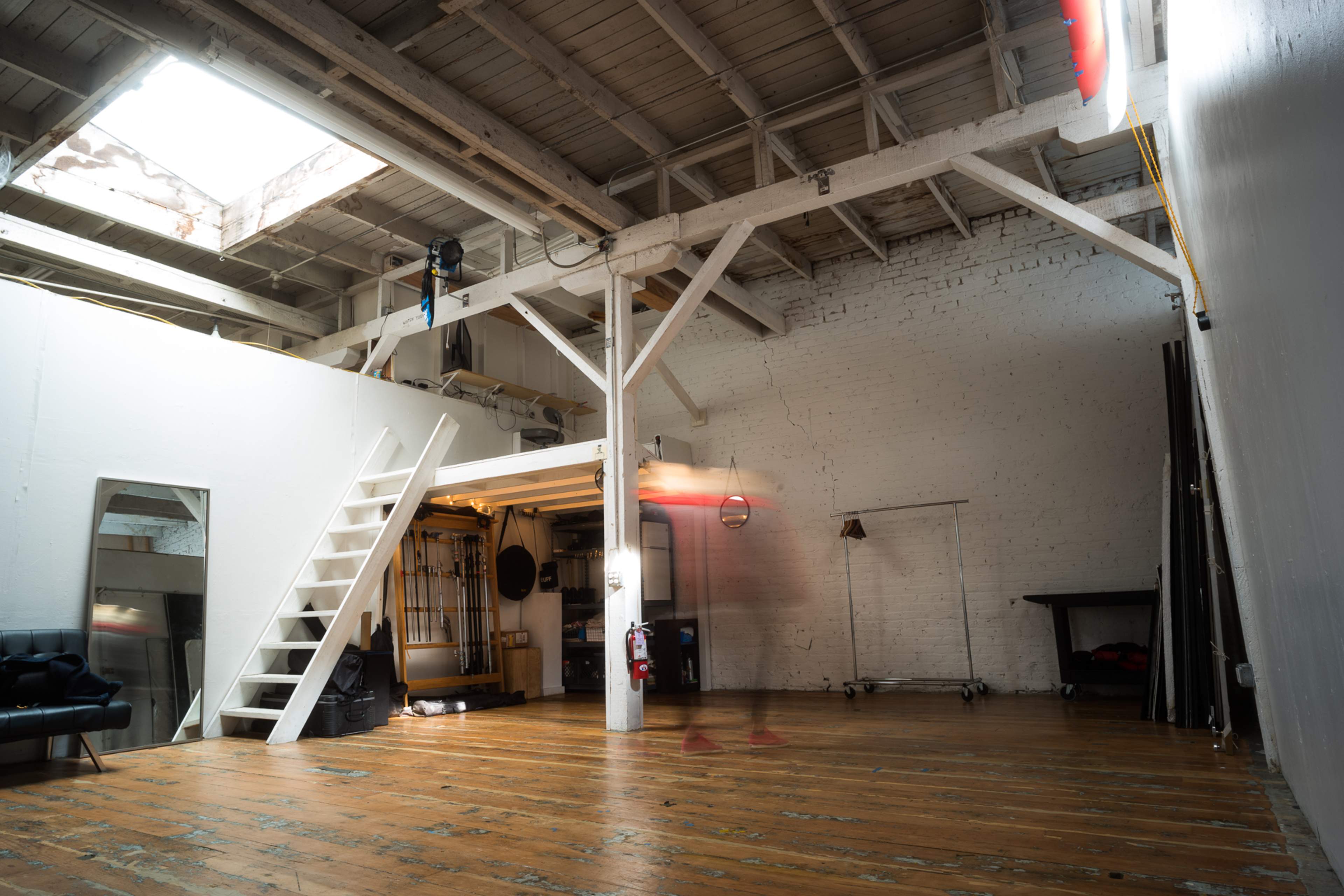 A spacious, industrial-style loft features wooden floors, exposed beams, and a staircase leading to a lofted area.