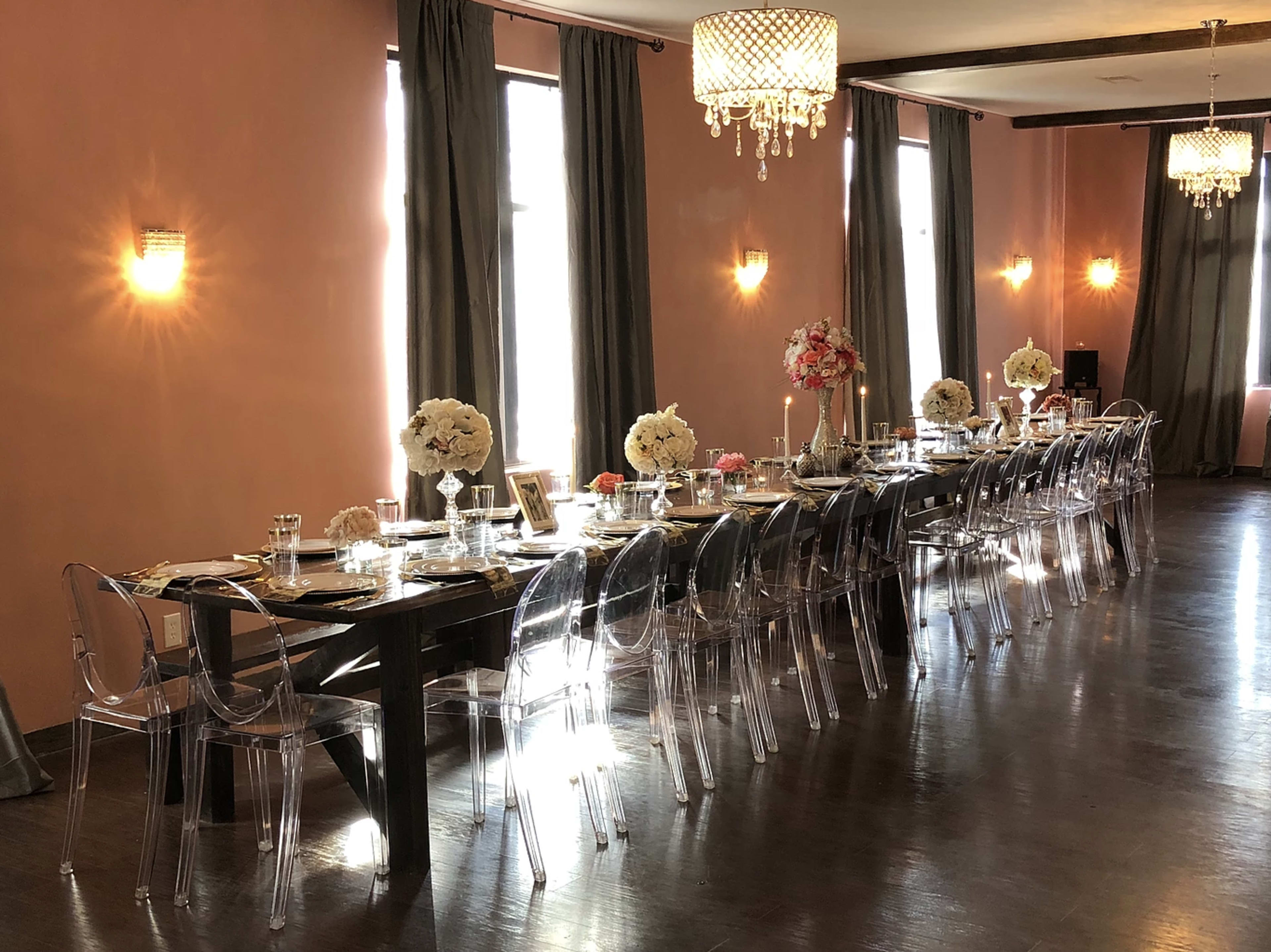 A long dining table is set with elegant tableware and floral centerpieces in a softly lit room featuring chandeliers and draped curtains.
