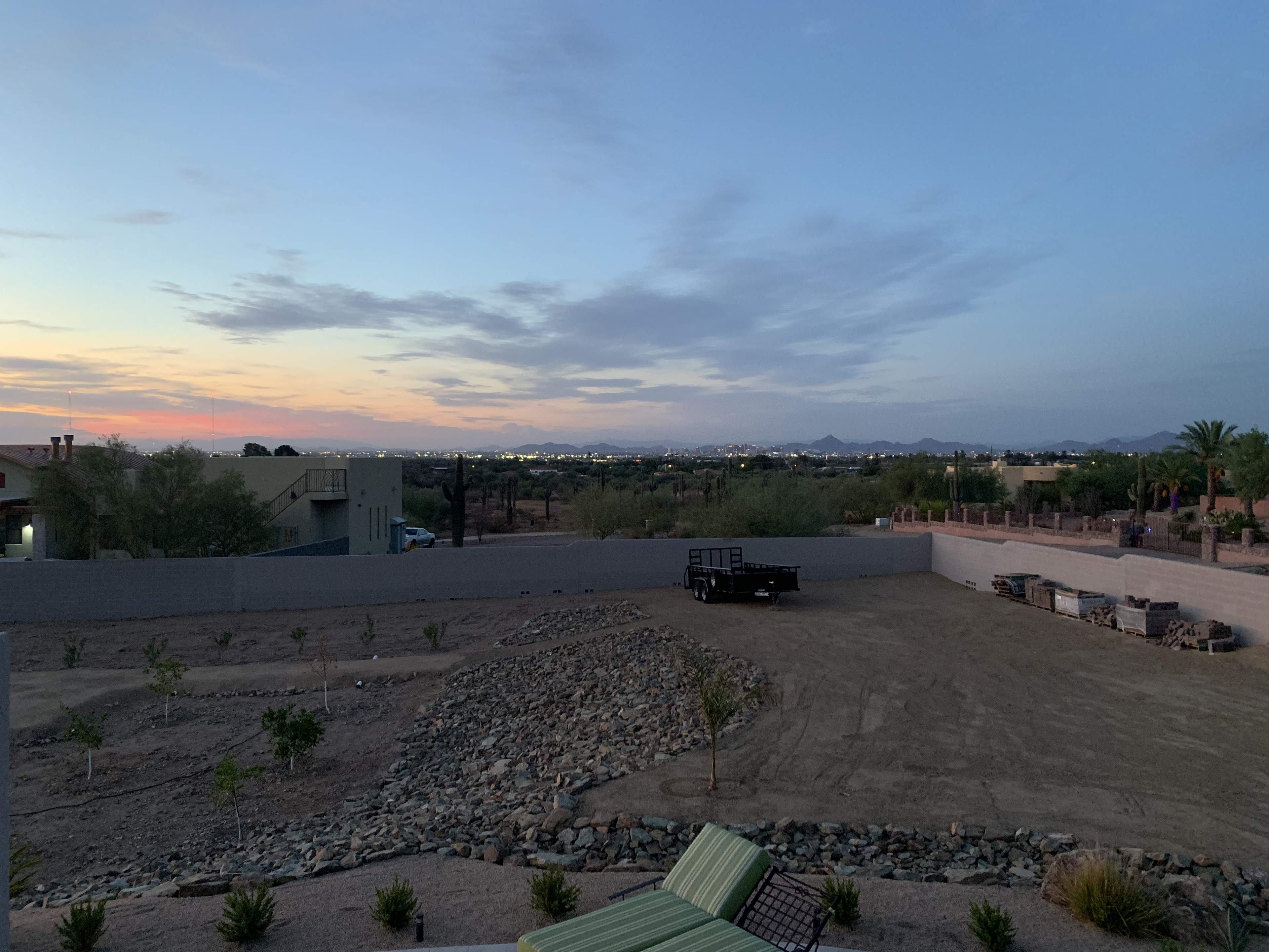 An expansive view of a largely barren landscape at twilight, with distant mountains and scattered lights in the background.