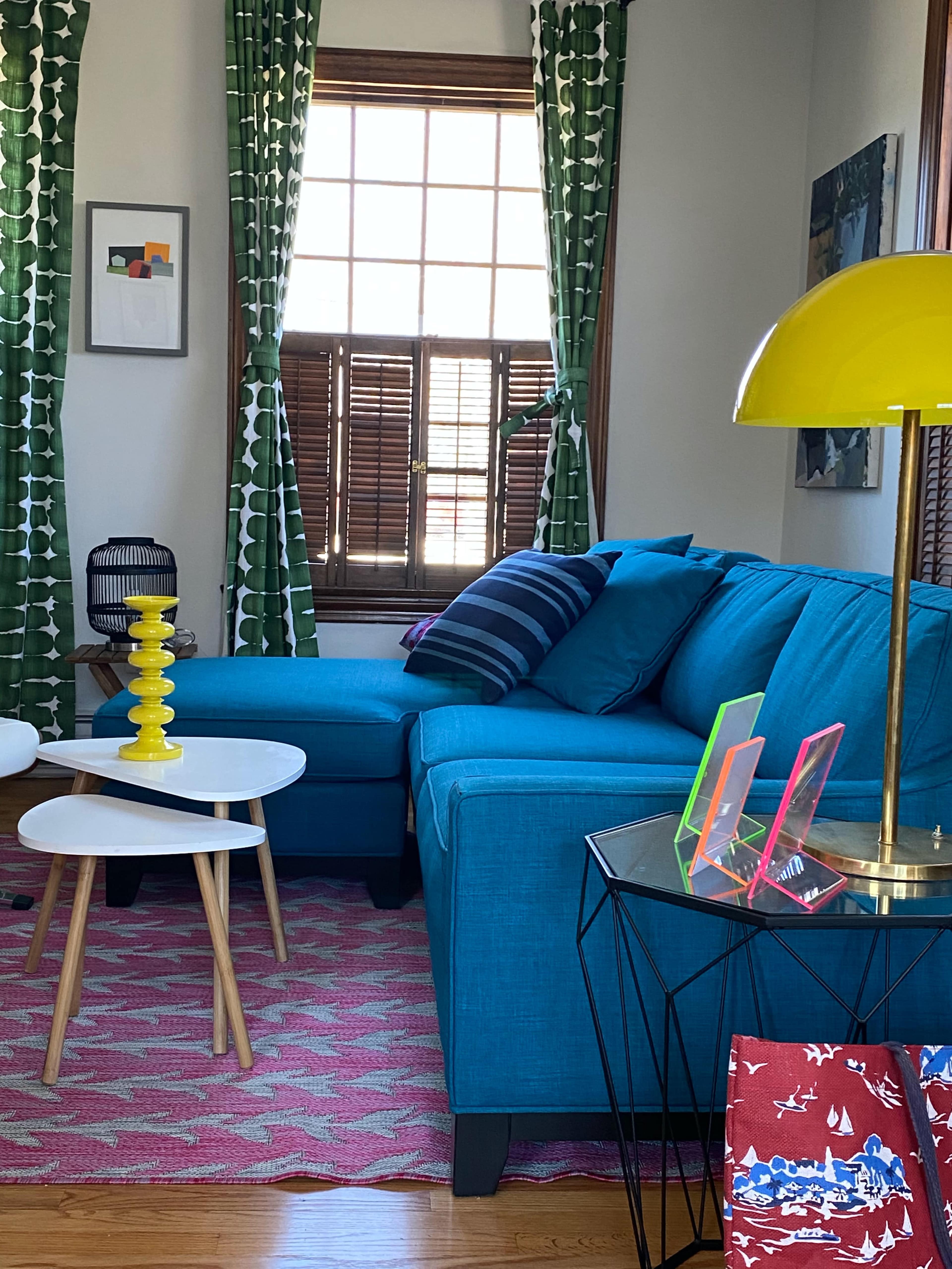A bright living room features a blue sectional sofa, a white coffee table, and decorative items on a pink area rug.