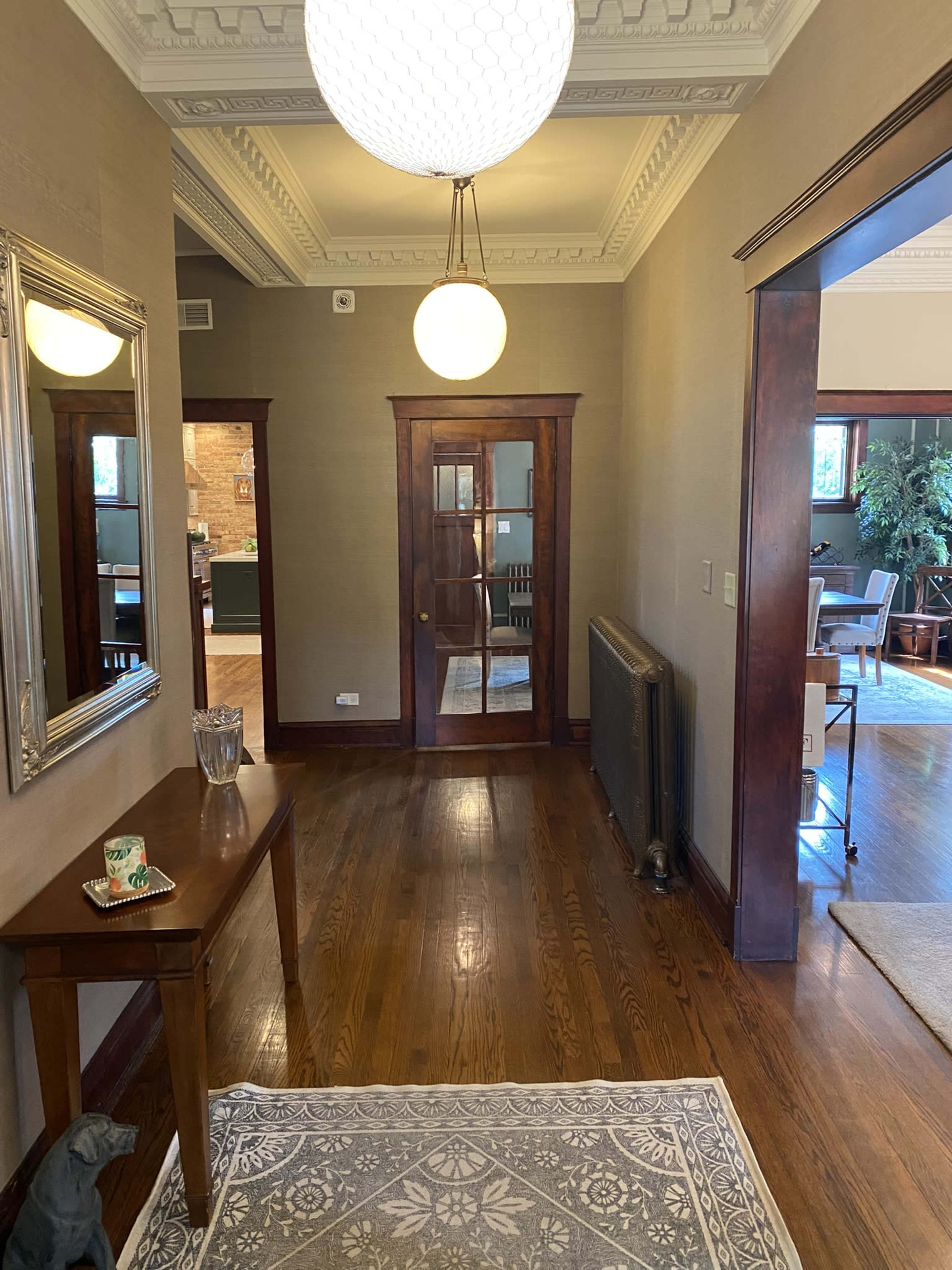 The hallway features a hardwood floor, a round light fixture, a mirror on the wall, and a door leading to another room.