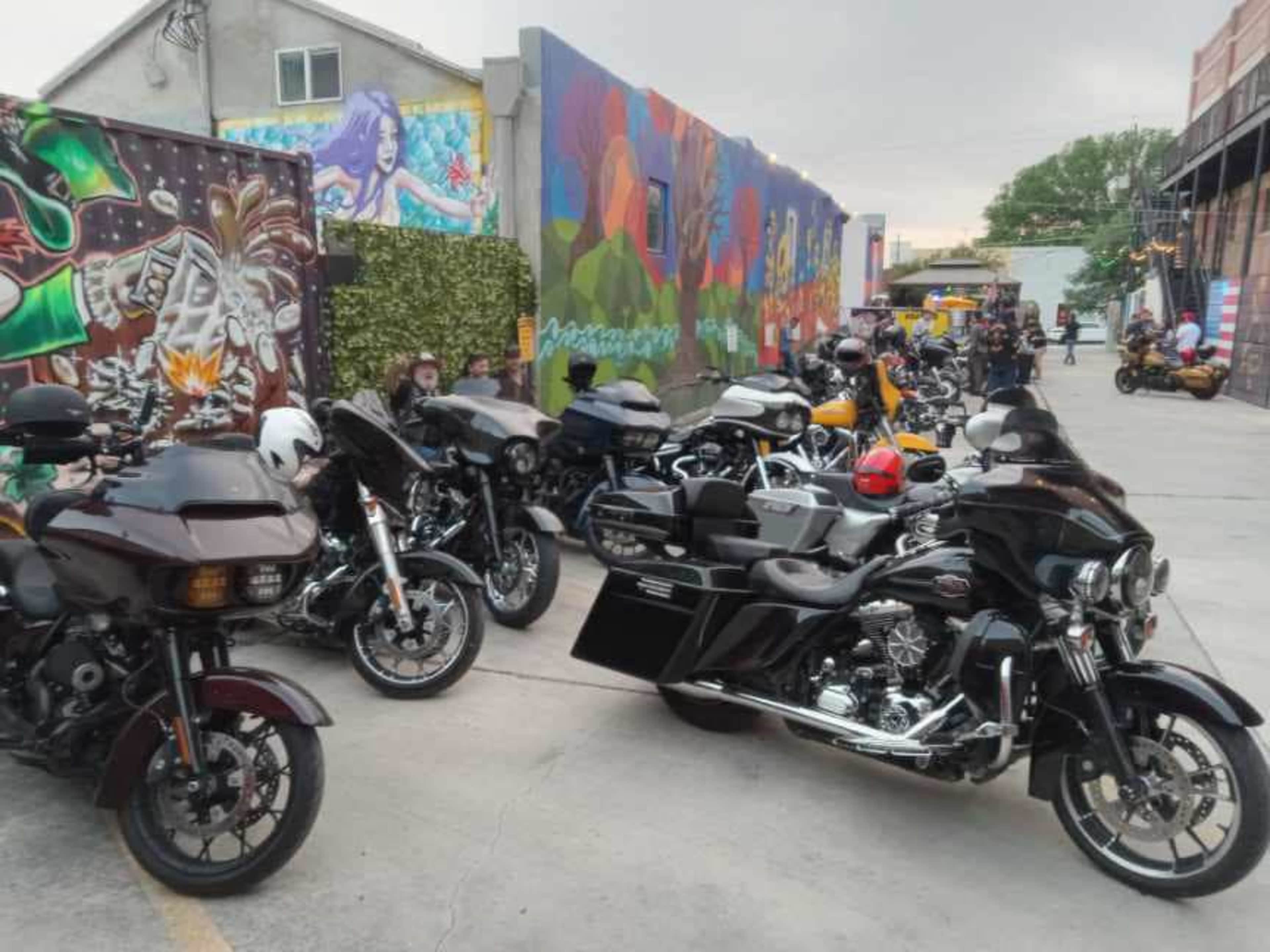 A row of various motorcycles is parked in front of a colorful mural with graffiti art on a street.