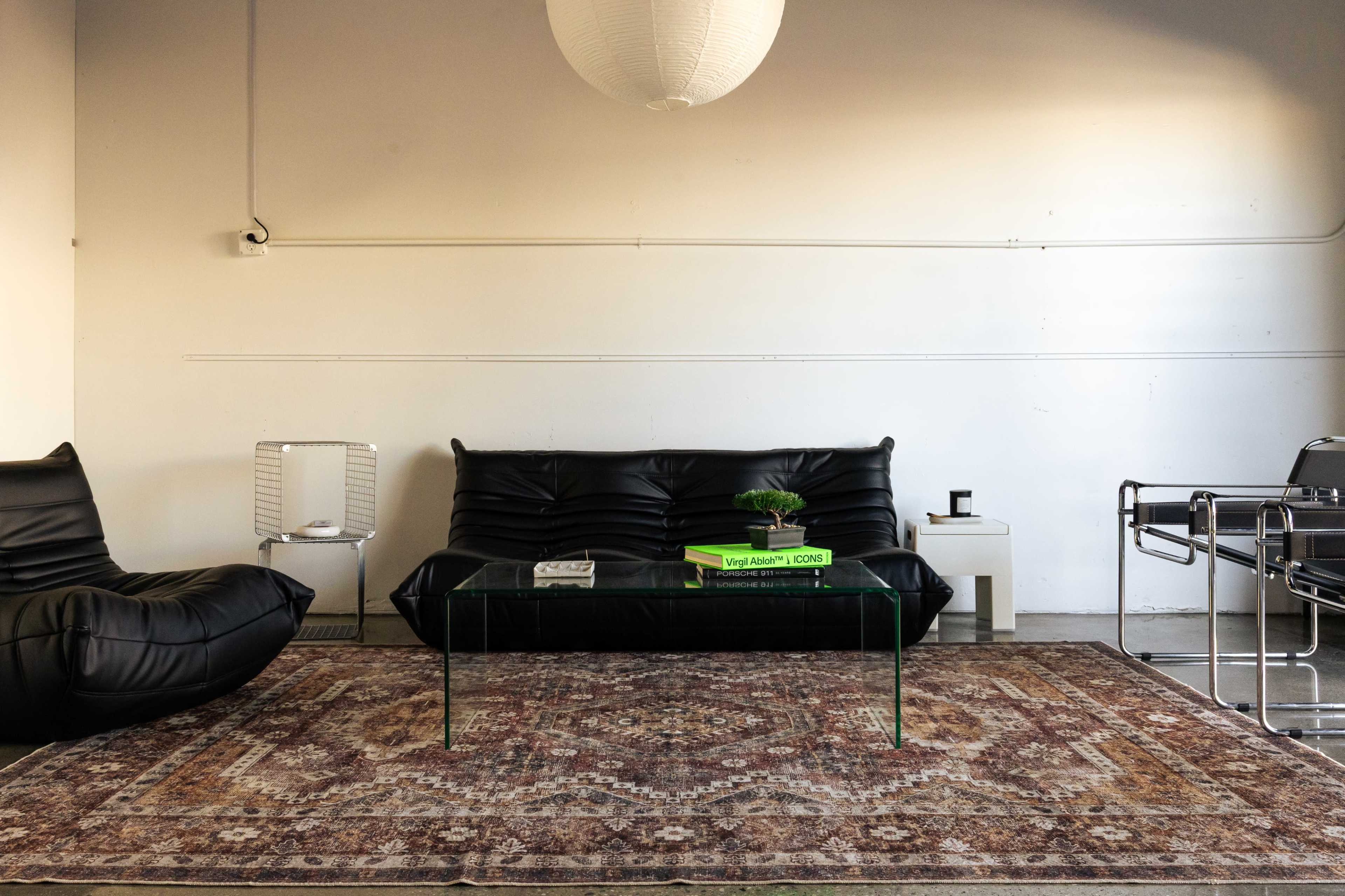 The scene features a modern living area with black leather furniture, a glass coffee table, and a patterned area rug.