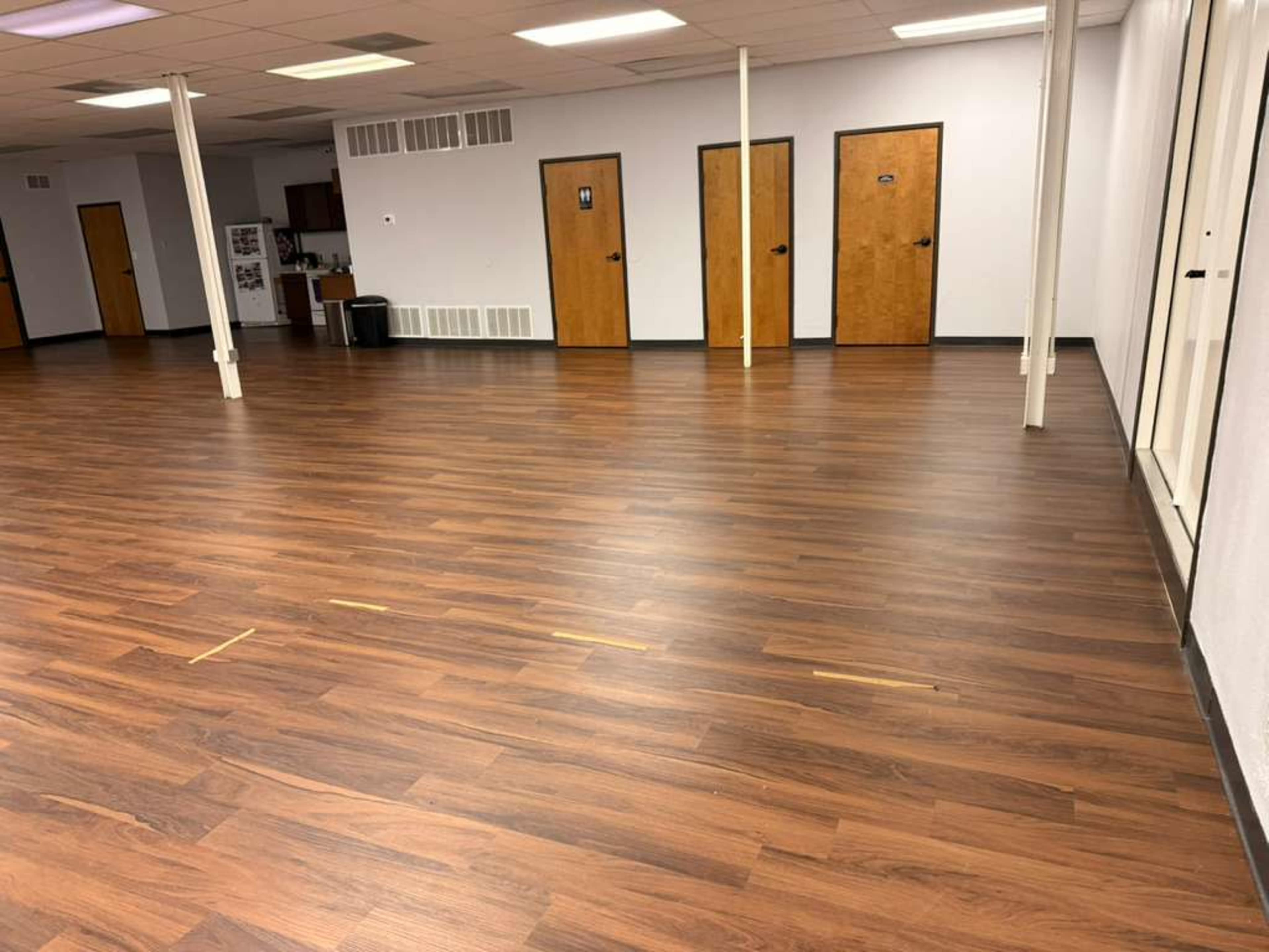 The image shows a large, empty interior space with wooden flooring and several closed doors along the walls.