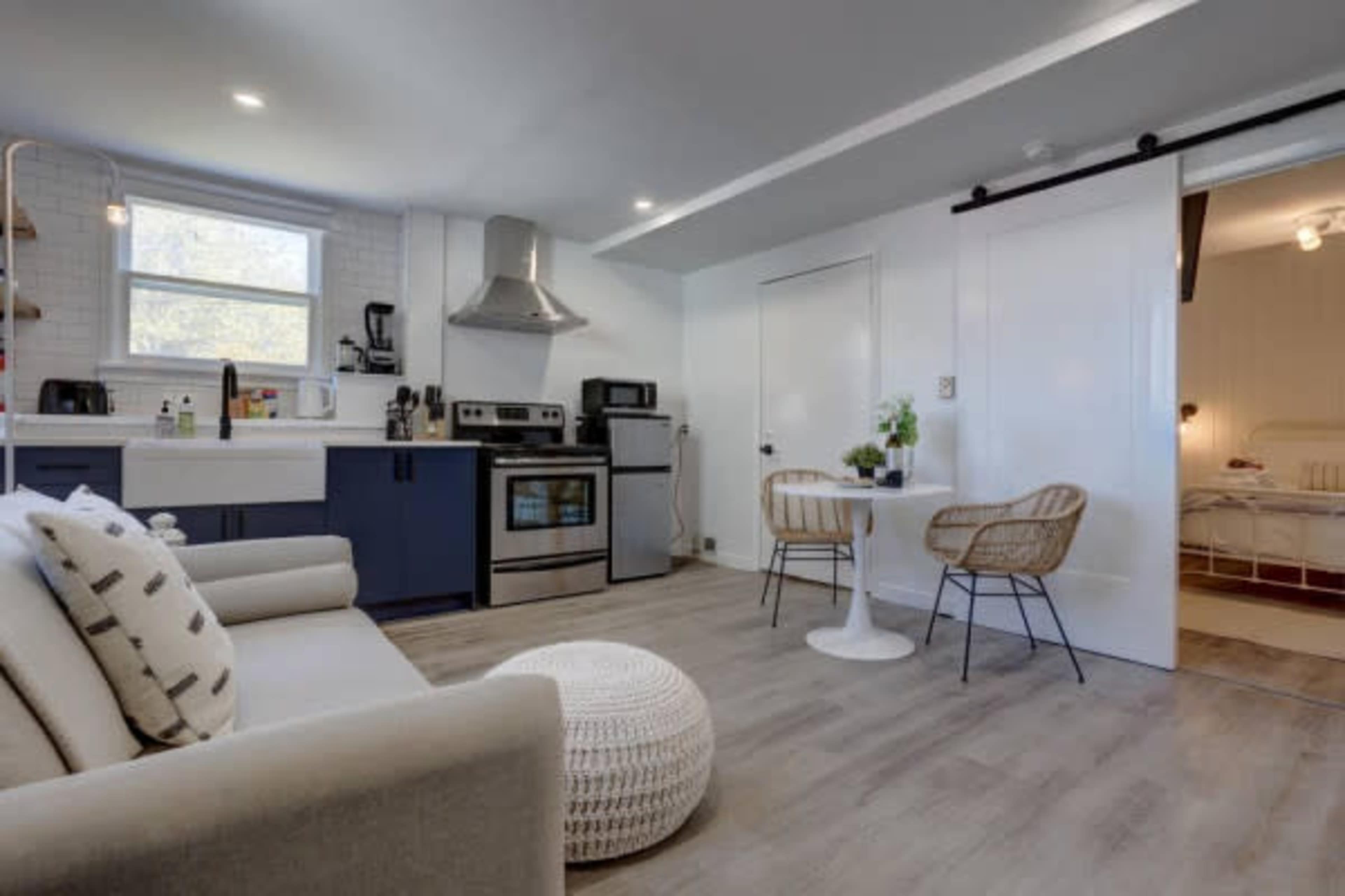 A modern kitchen and living area featuring a sofa, a dining table for two, and stainless steel appliances.