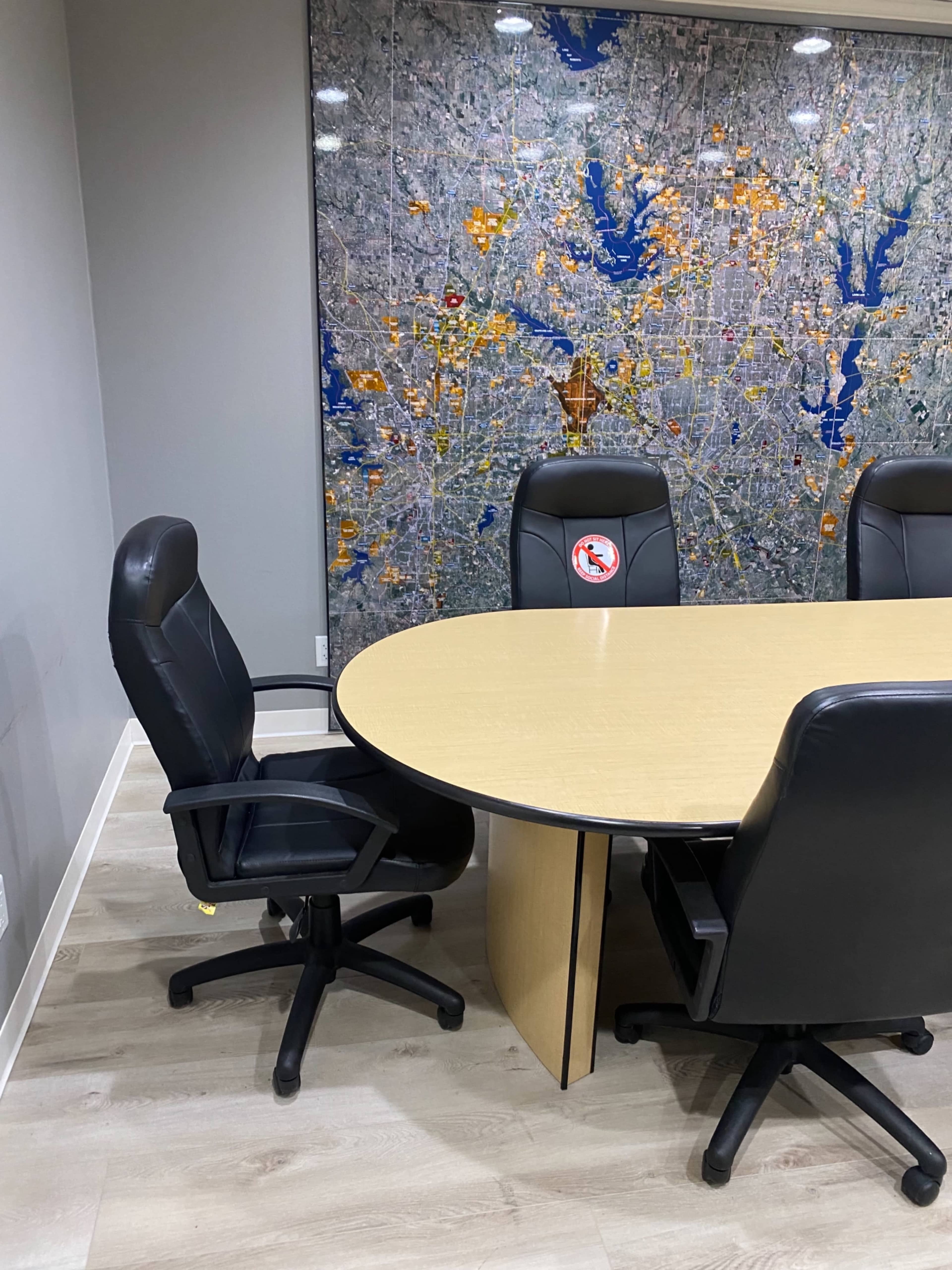 A conference room features a round table with black swivel chairs and a large wall map in the background.