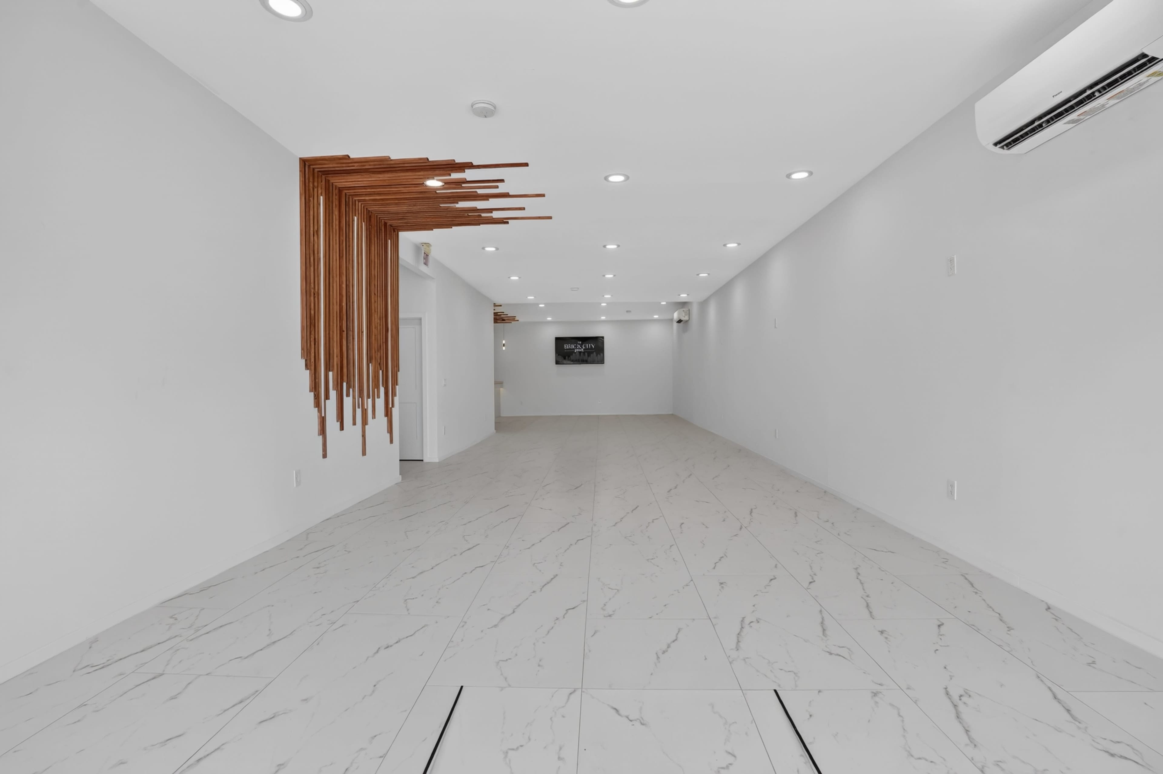 The image shows a spacious, modern interior with white walls, marble-like tiled flooring, and a decorative wooden feature on one side.